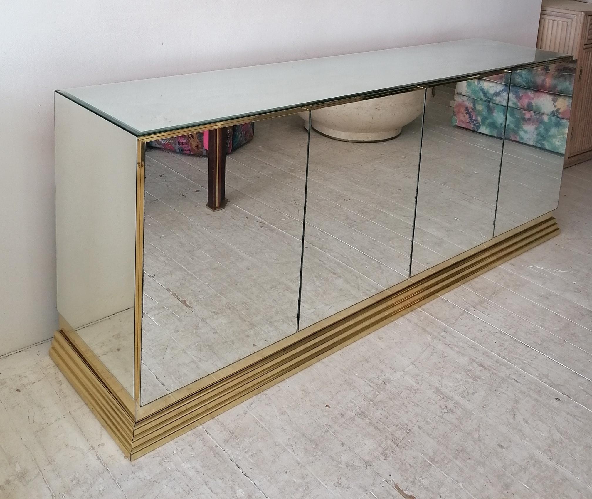 A stunning mirrored sideboard by Ello Furniture, USA 1980s. Bevelled mirror glass  top & mirror glass doors and ends, gold metal plinth base. Inside are 2 adjustable shelves and one drawer.
There's some age-related foxing to the mirror glass... Not