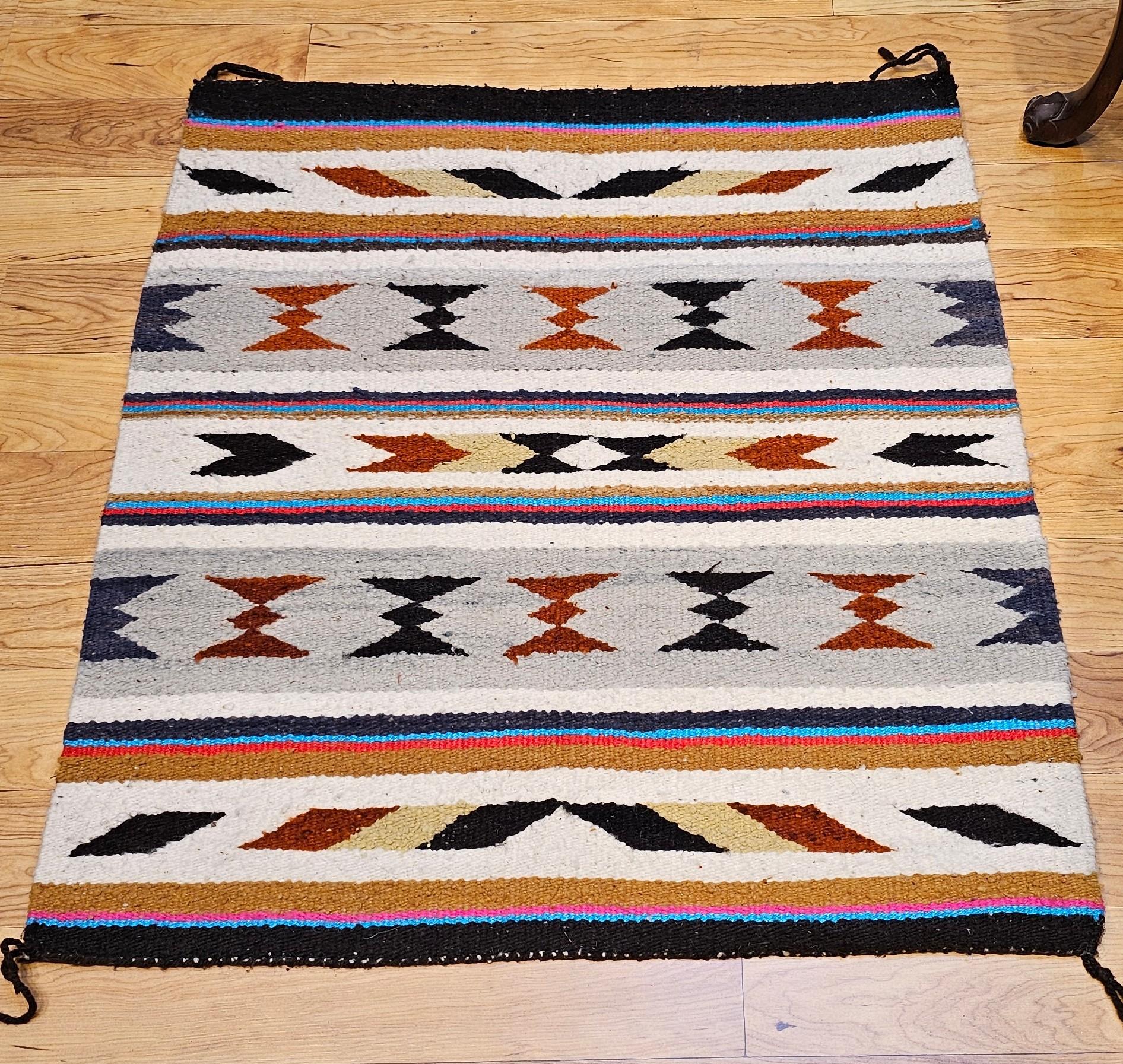 Questa coperta da sella vintage dei nativi americani Navajo, tessuta a mano nel terzo quarto del XX secolo, presenta un classico disegno a righe intervallato da bande alternate di intricati motivi geometrici. Eseguito in una tavolozza senza tempo di