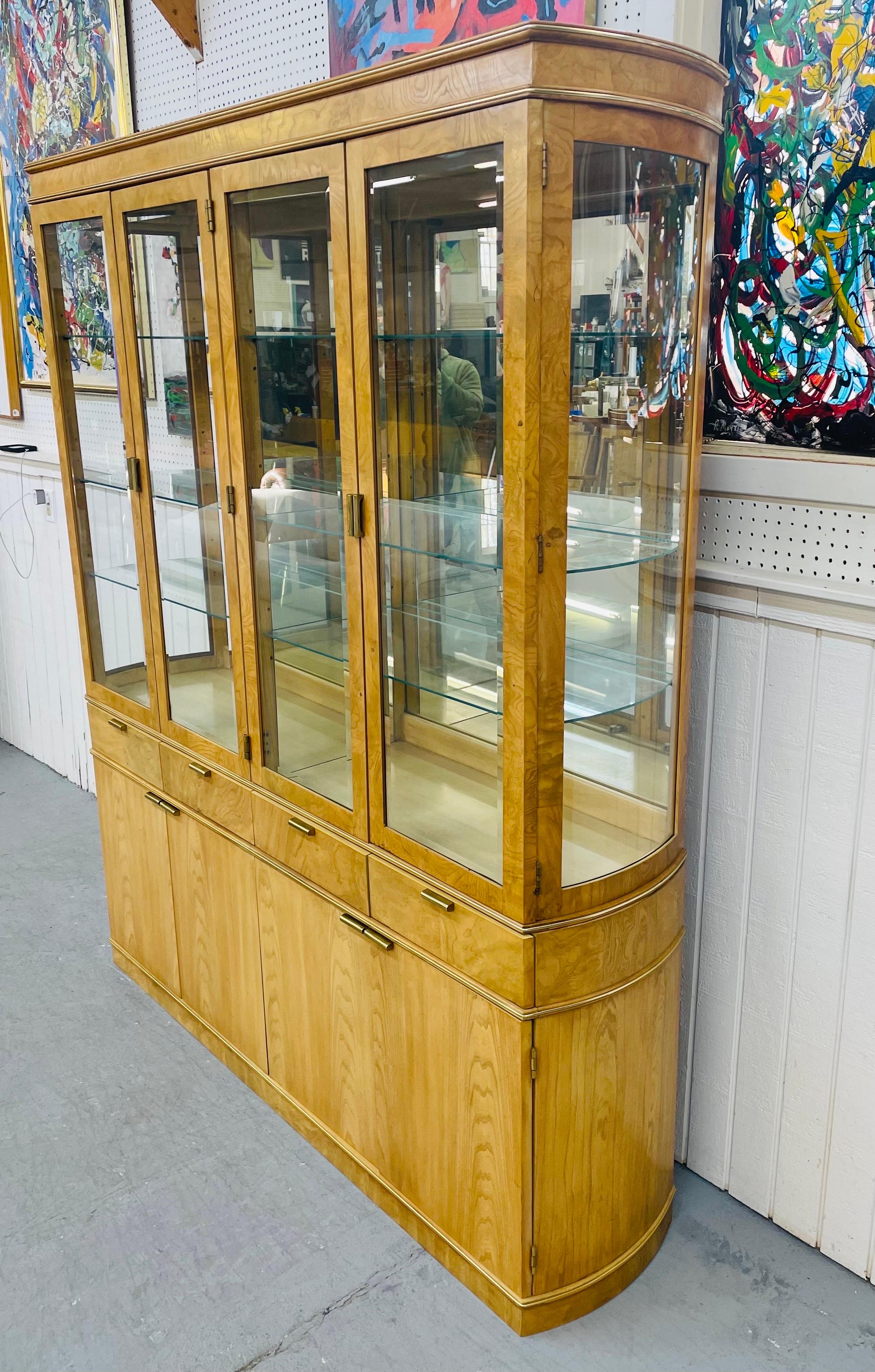 This listing is for a vintage American of Martinsville Burled Breakfront. Featuring four glass doors that open up to glass shelves, interior lights, four wood doors at the bottom that open up to a shelf, four drawers that open up for more storage,