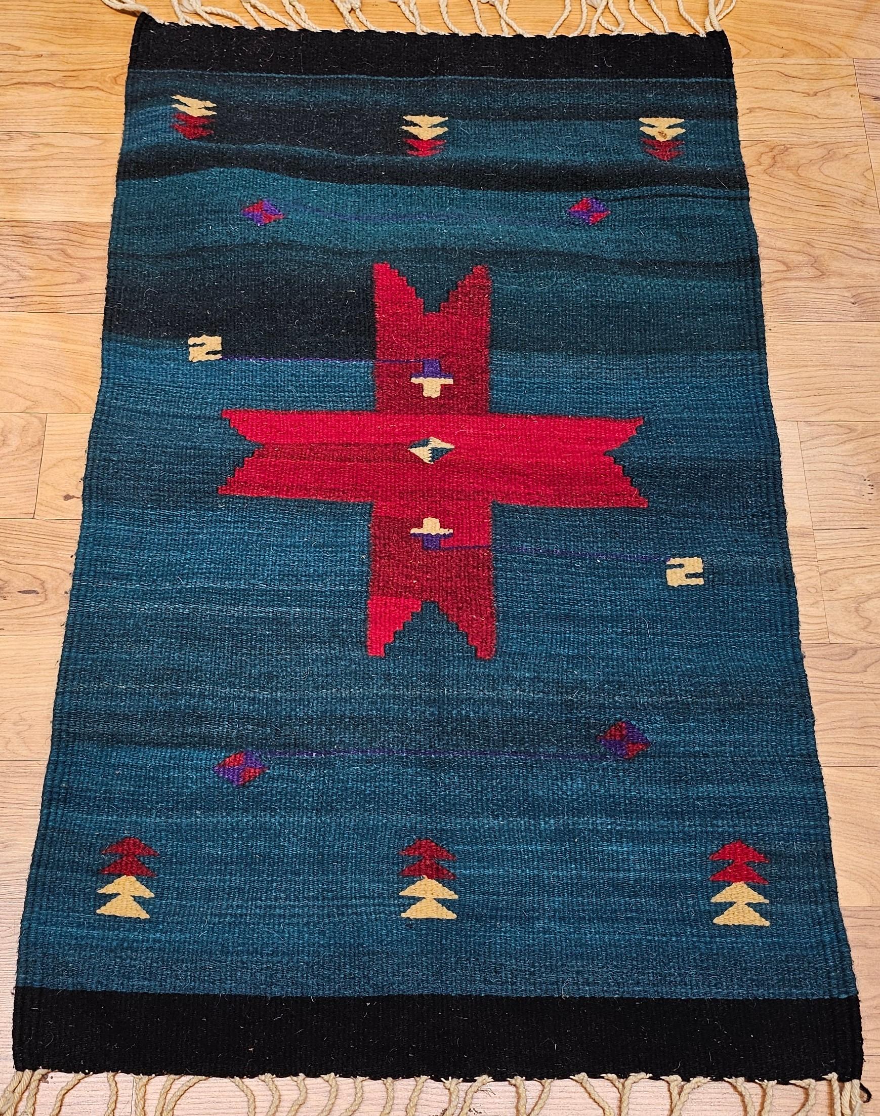 This vintage American Southwestern kilim rug, handwoven in the late 20th century, beautifully captures the essence of traditional Southwestern textile art. Featuring a bold dark green field, the rug is centered with a striking red medallion,