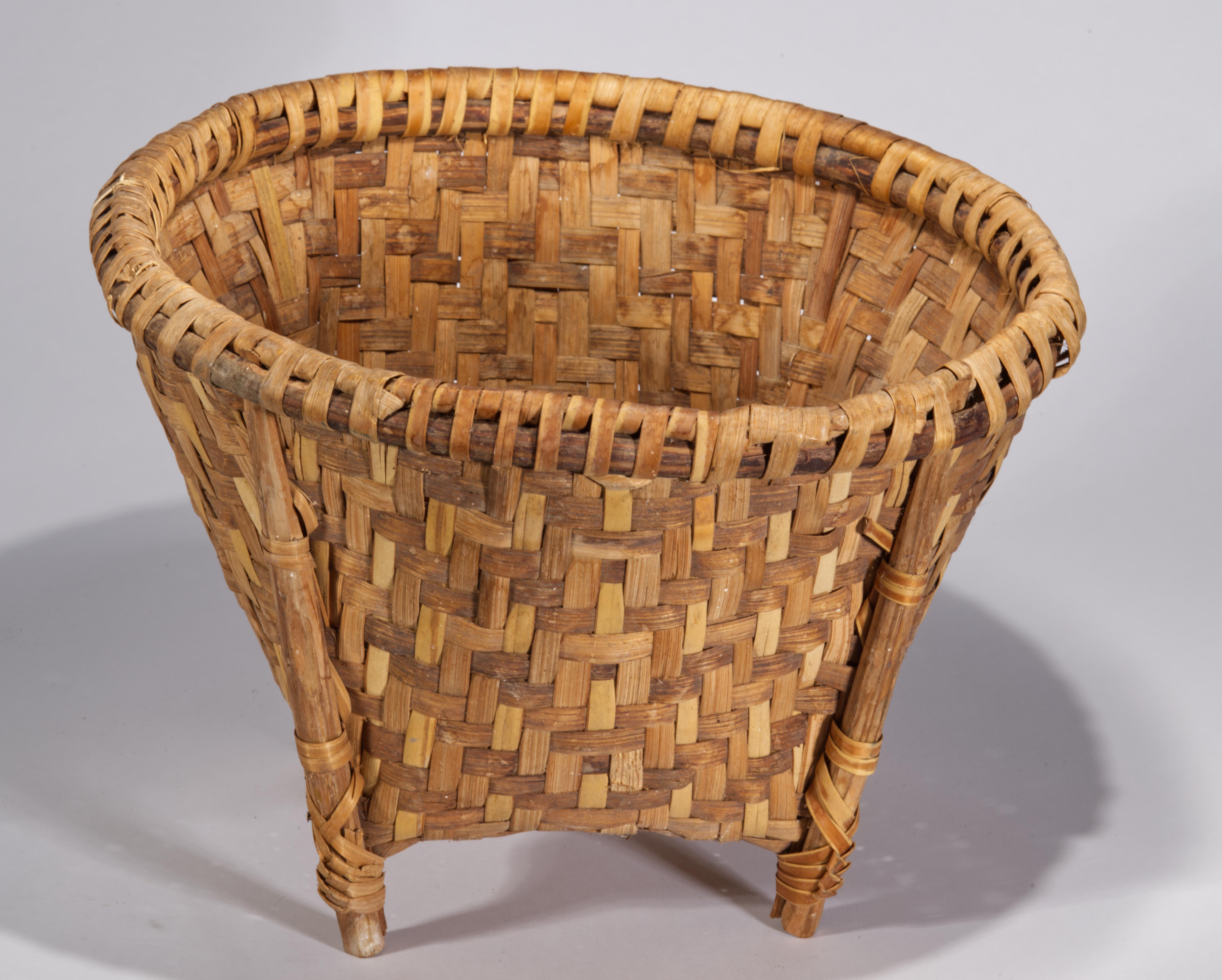 Il cestino vintage è caratterizzato da una base quadrata e da una parte superiore arrotondata. Il piano è rinforzato da pezzi di legno curvato intagliati, avvolti da stecche; quattro gambe di legno intagliato sono attaccate al bordo di legno del