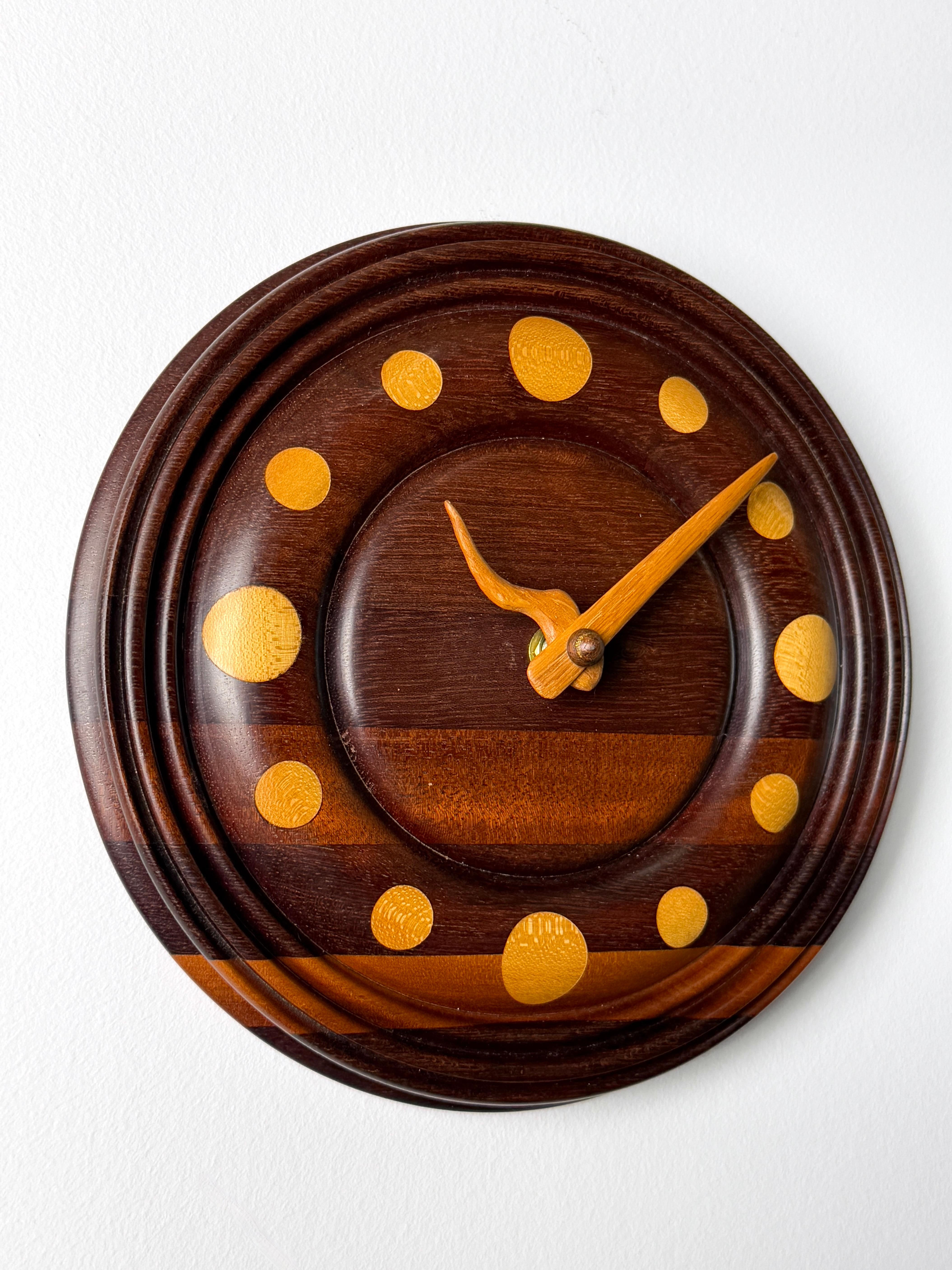 Horloge murale ronde en bois, unique en son genre, réalisée par un artiste. 
Circa 1980

Design/One en bois mélangé magnifiquement tourné avec des marqueurs incrustés contrastés et fini avec des mains sculptées uniques.

Le mouvement de la batterie