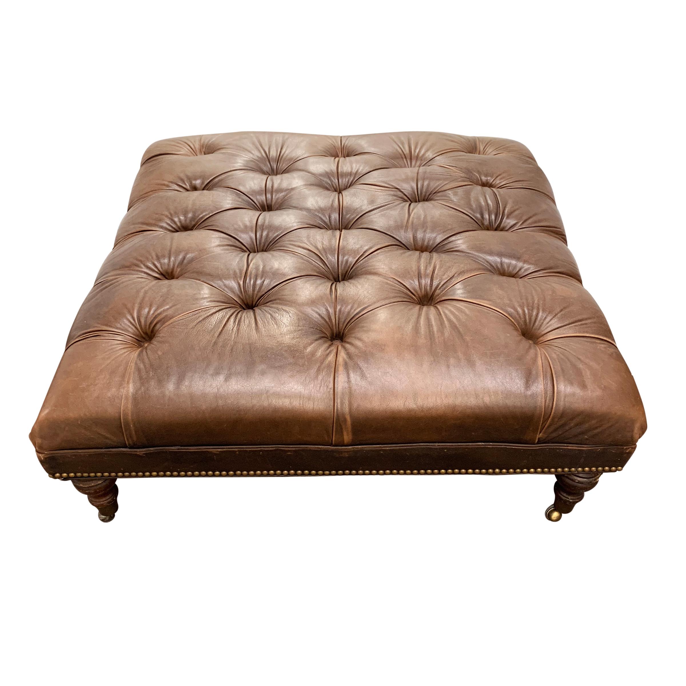 A vintage American tufted leather ottoman of large size with brass nailhead trim and turned wood legs on casters.