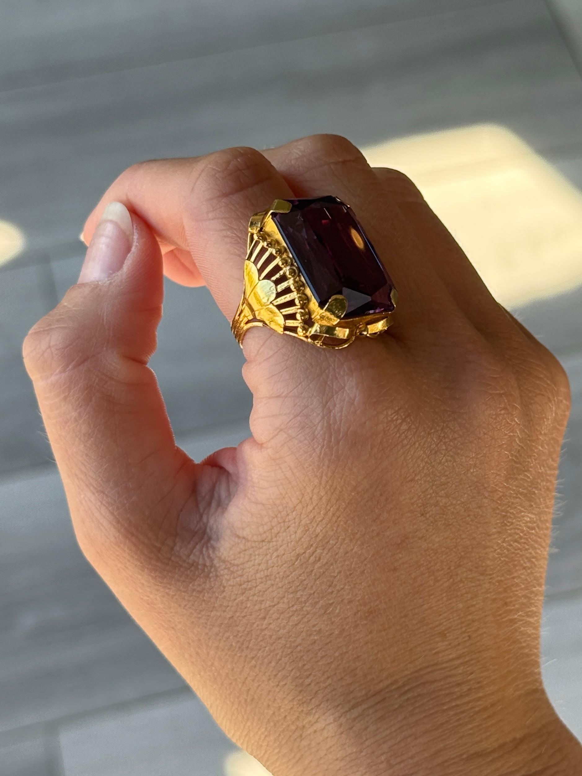 Questo splendido anello da cocktail contiene un'ametista di colore viola lucido e brillante, a tratti con riflessi blu. La pietra è trattenuta da ampie griffe e il resto dell'anello è ornato e modellato in oro 22ct. 

Misura dell'anello: Q o