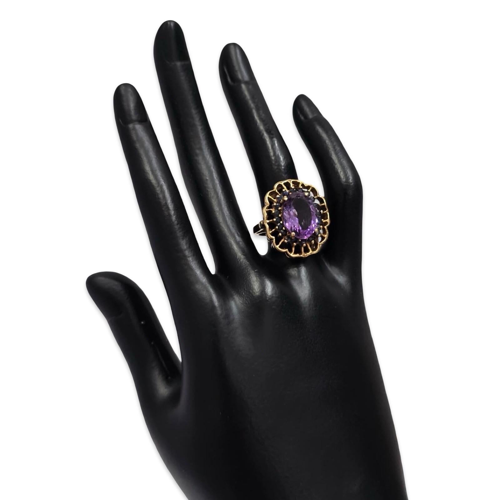 Uno squisito anello cocktail d'epoca in oro giallo 10K, disegnato intorno a una vibrante ametista ovale da 5,5 carati che misura 14 × 10 mm, circondata da 20 zaffiri blu rotondi di circa 0,04 carati ciascuno, per un totale di circa 0,80