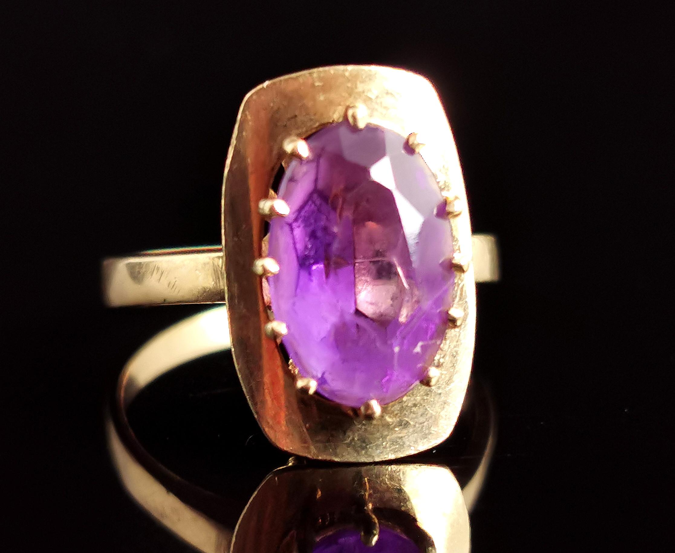 A Gorgeous vintage Amethyst cocktail ring.

This beautifully designed 1970s era cocktail ring has a large gold setting set to the centre with a vibrant oval cut purple Amethyst.

It is prong set and has a slightly abstract brutalist setting.

It has