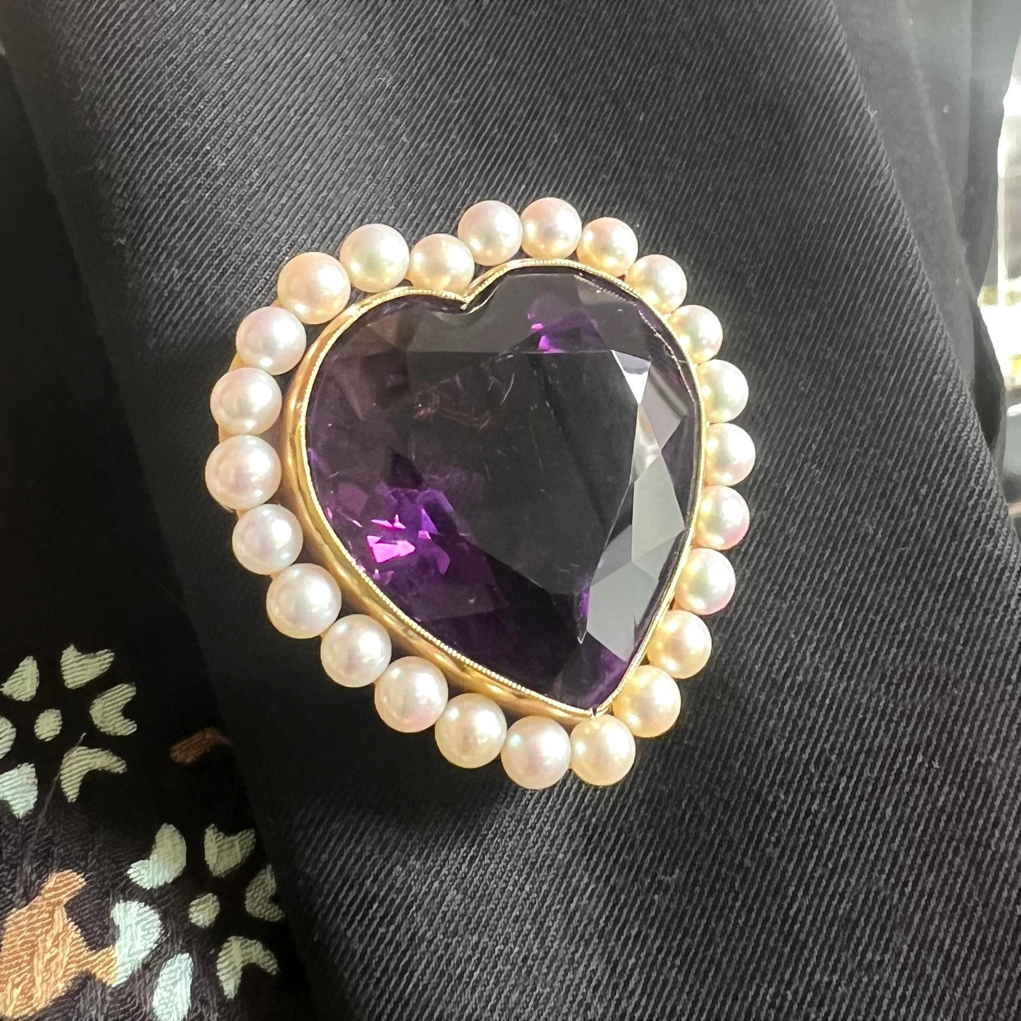 A vintage amethyst and cultured pearl heart brooch-cum-pendant, set with a large, faceted, heart shaped amethyst, in a millegrain edged rub over setting, surrounded by 24 cultured pearls, mounted in 14ct gold, with a pin with a safety hook, with a