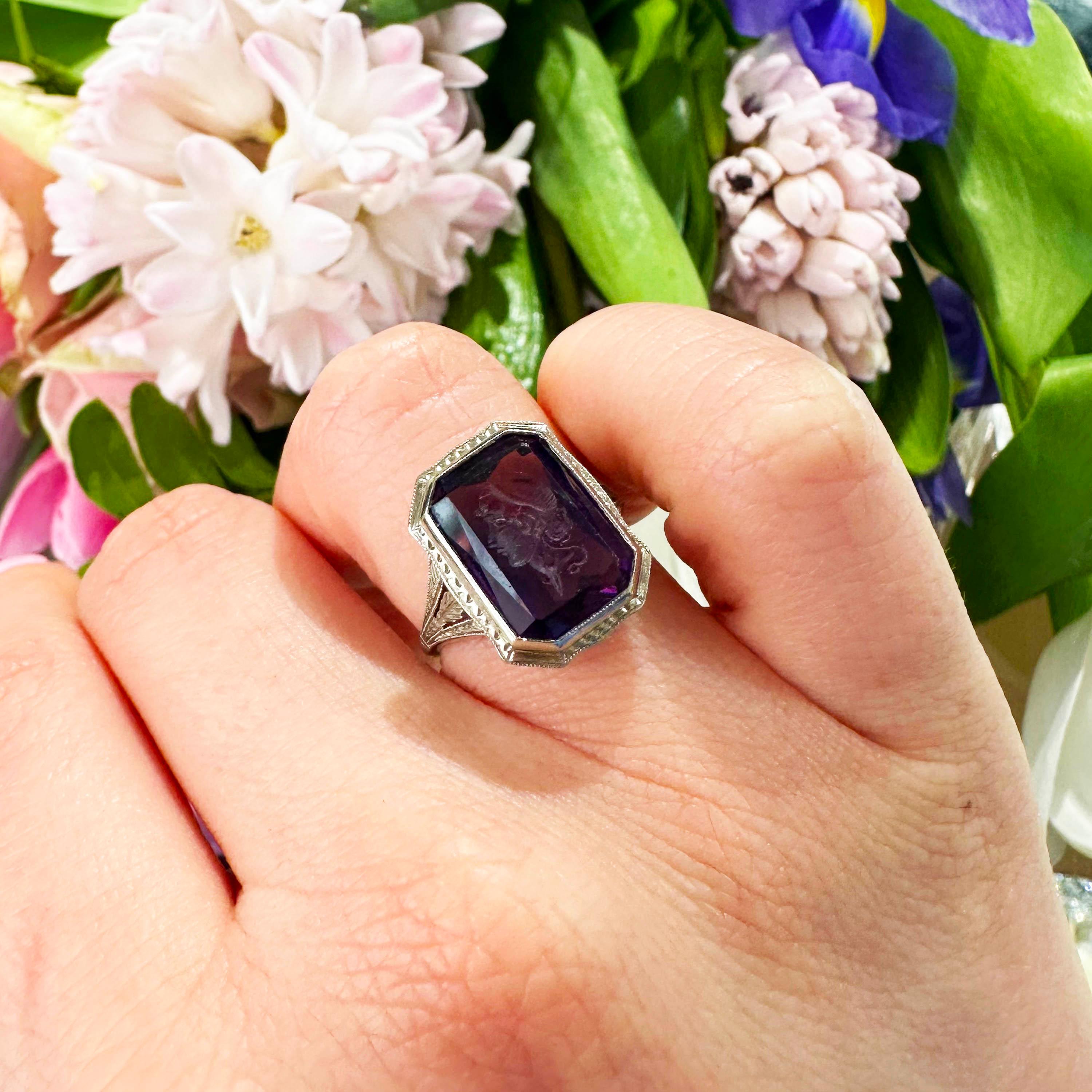 An amethyst intaglio ring, with an emerald-cut amethyst, carved with the head of a Roman style woman, in a millegrain edged rub over setting, with a square nailhead design and millegrain edged surround, with carved and millegrain trefoil shoulders,