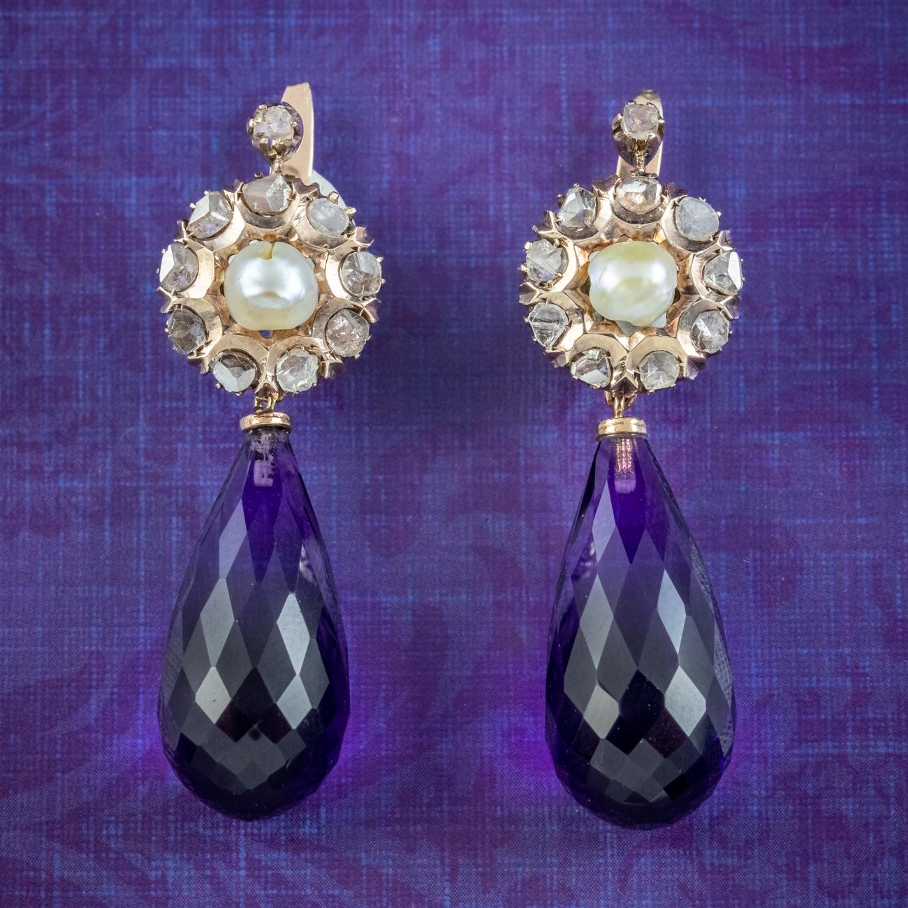 A glamorous pair of vintage drop earrings (Circa 1930) adorned with luxurious briolette cut amethyst droppers with a deep, regal purple hue (approx. 20ct each). The tops are fashioned in 14ct gold with a central pearl and a halo of flickering rose