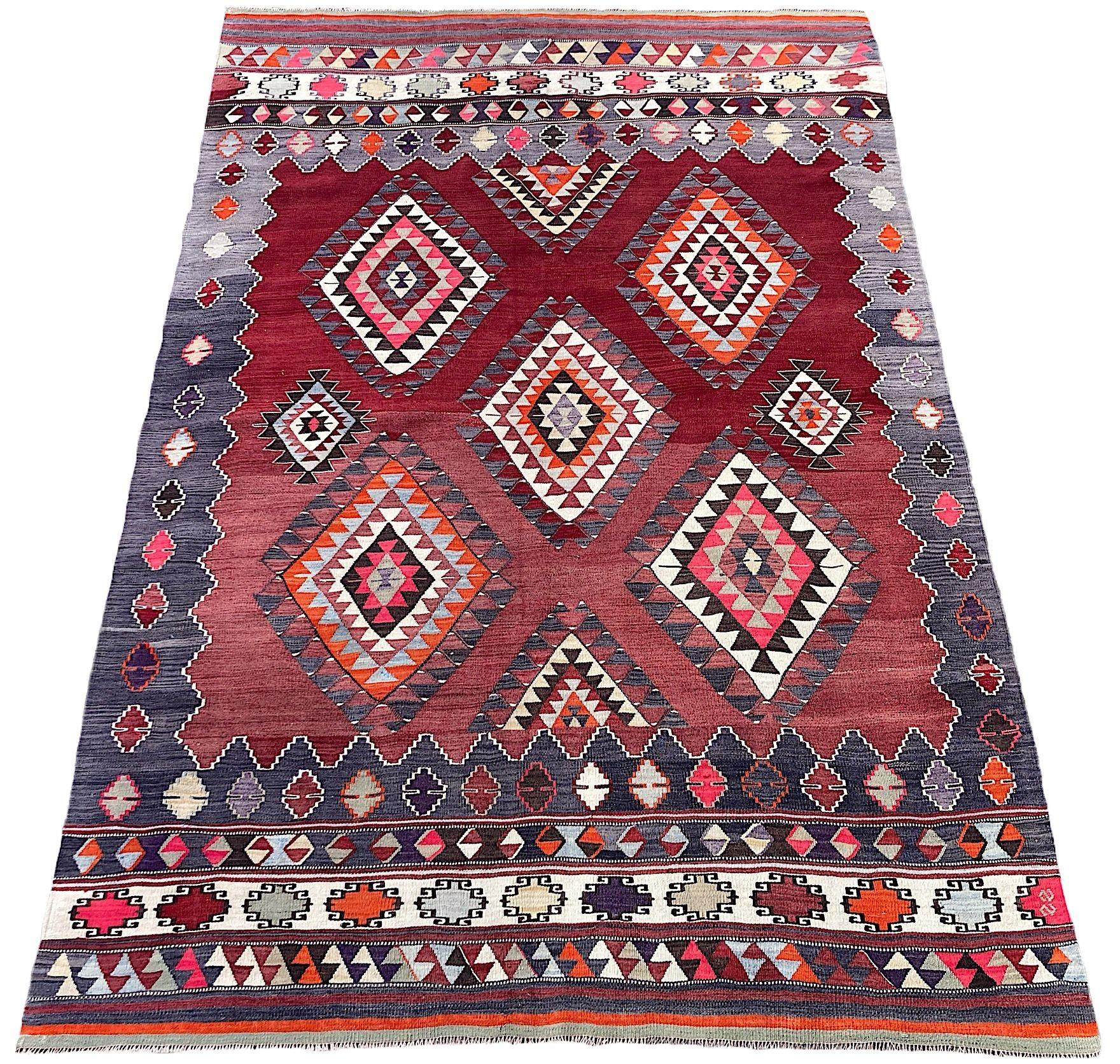 A beautiful vintage Anatolian kilim, handwoven in the mid 20th Century in the region of Dursunbey, north-west Turkey. The kilim features an all over geometrical design of random medallions on a rich abrasched red field surrounded by a soft grey