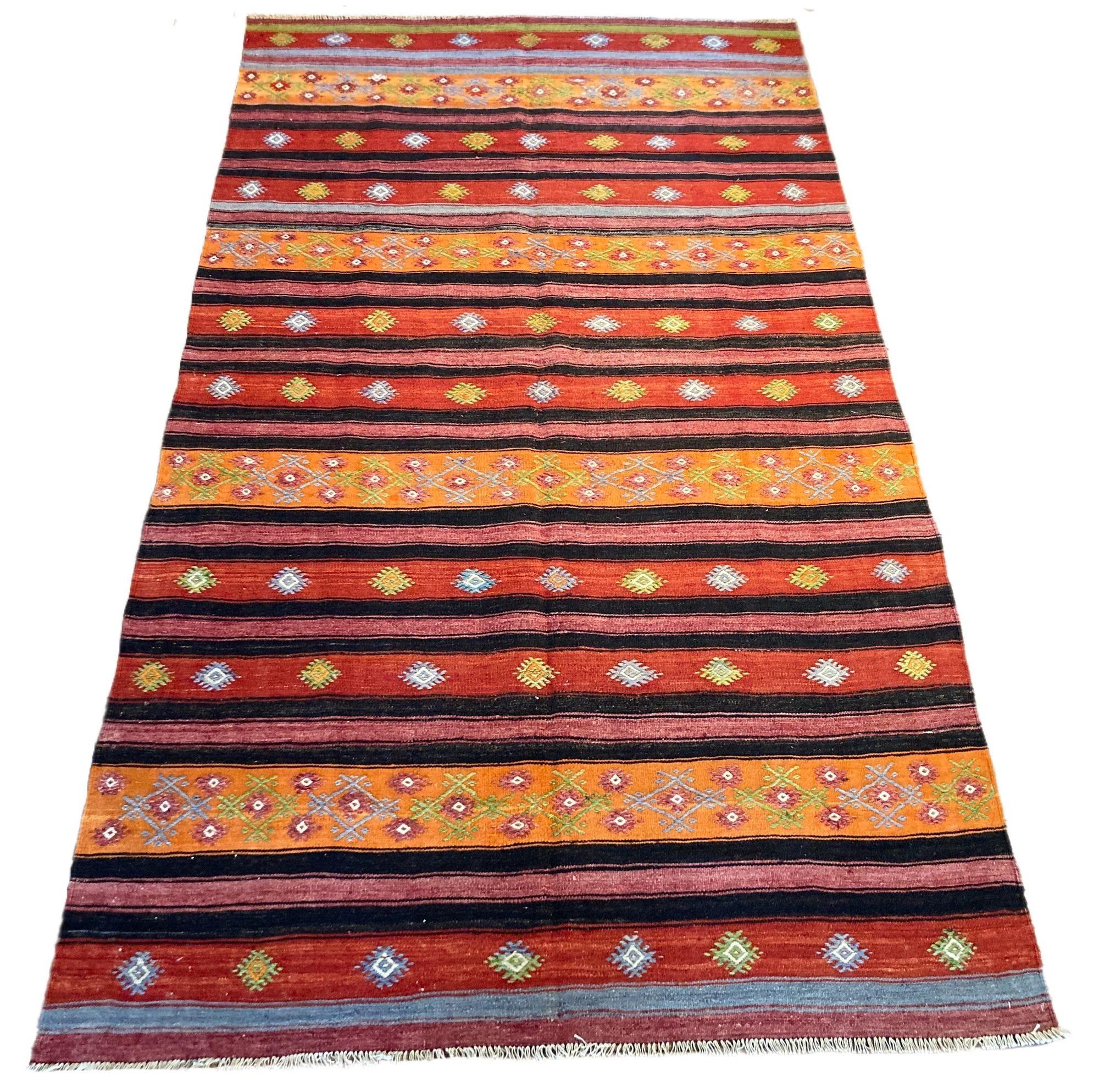 A beautiful vintage kilim, handwoven in central Turkey circa 1960 featuring a multicoloured banded design in red, orange, charcoal and blue.
Size: 3.03m x 1.70m (9ft11in x 5ft 7in)
This kilim is in good condition with light, age related wear. The