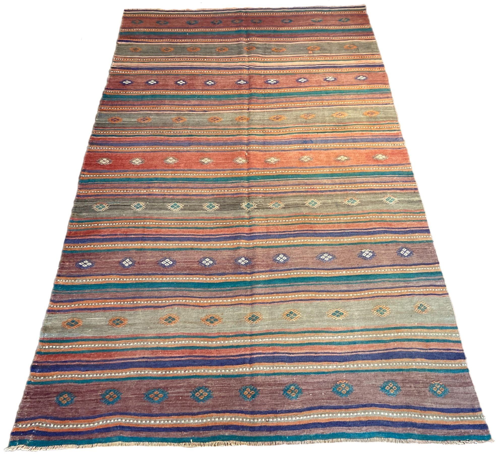 A beautiful vintage kilim, handwoven in central Turkey circa 1960 featuring a multicoloured banded design in aubergine, terracotta and turquoise.
Size: 3.38m x 1.98m (11ft 1in x 6ft 9in)
This kilim is in good condition with light, age related