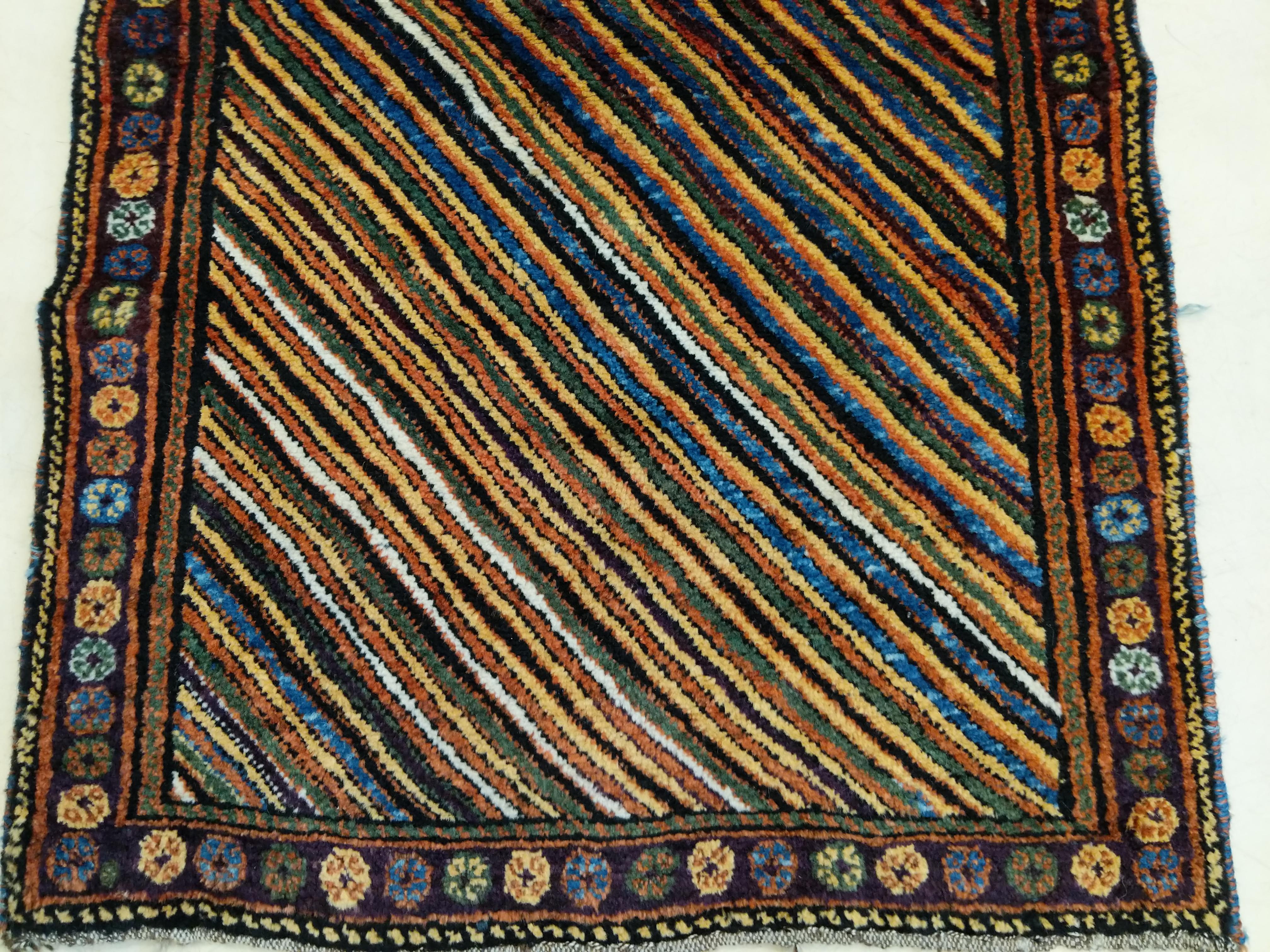 Ein kurdischer Stammesteppich, der sich durch ein Regenbogenmuster aus polychromen Diagonalen auszeichnet, das von einer einfachen Bordüre aus kleinen Oktogonen eingerahmt wird. Der weiche, üppige Flor ist typisch für die beste Qualität von