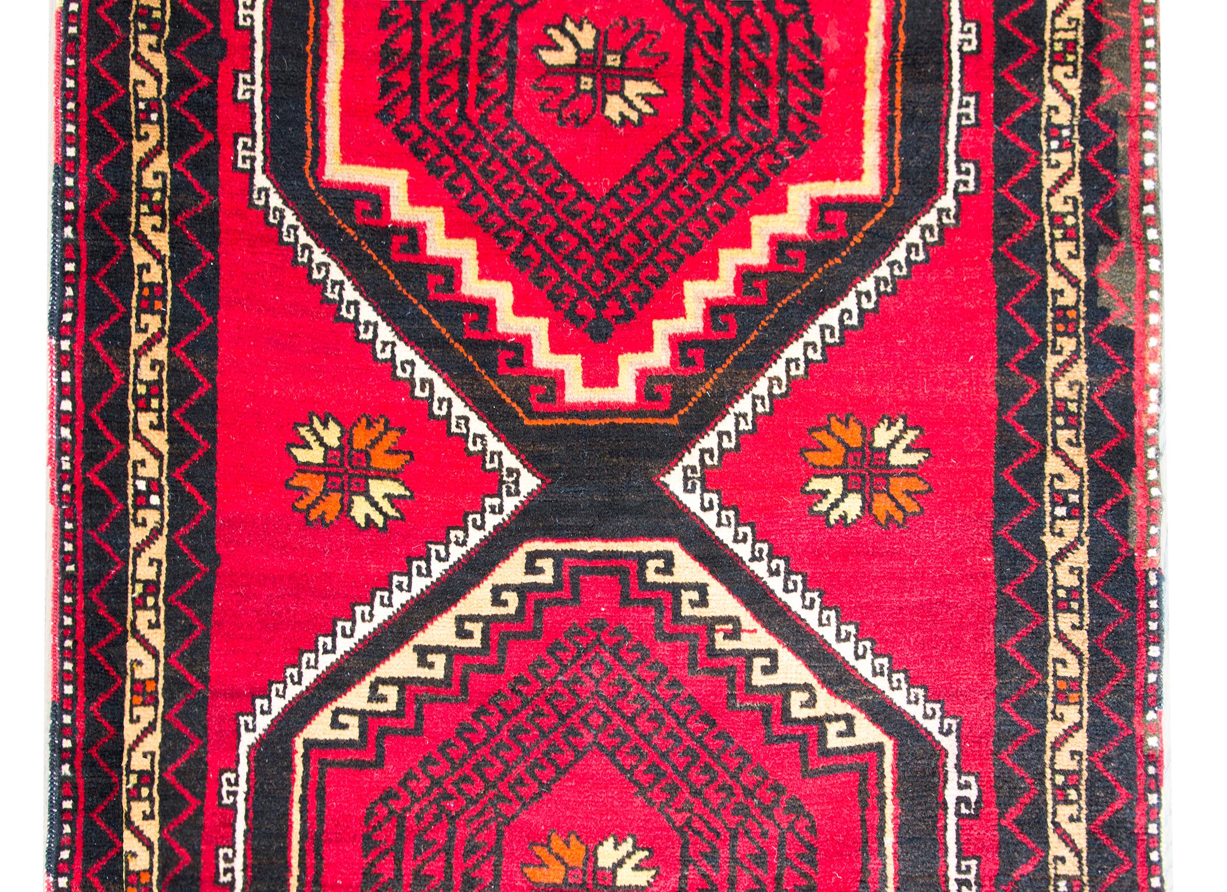 A bold Anatolian Turkish runner with three large diamond medallions with repeated concentric circles and living amidst a field of stylized flowers set against a rich crimson background, and surrounded by a complex border of multiple thin stripe