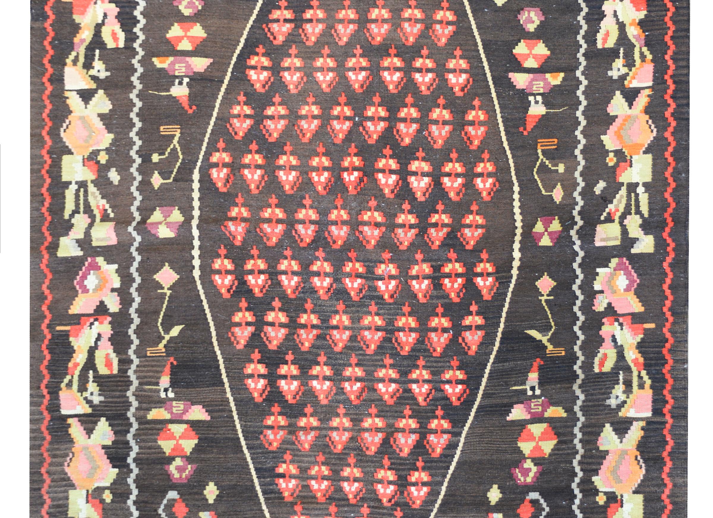 A beautiful vintage Anatolian Turkish kilim rug with a central diamond medallion with a red paisley pattern against a black background and surrounded by a stylized floral and scrolling vine pattern woven in pale greens, yellows, reds, and violets.