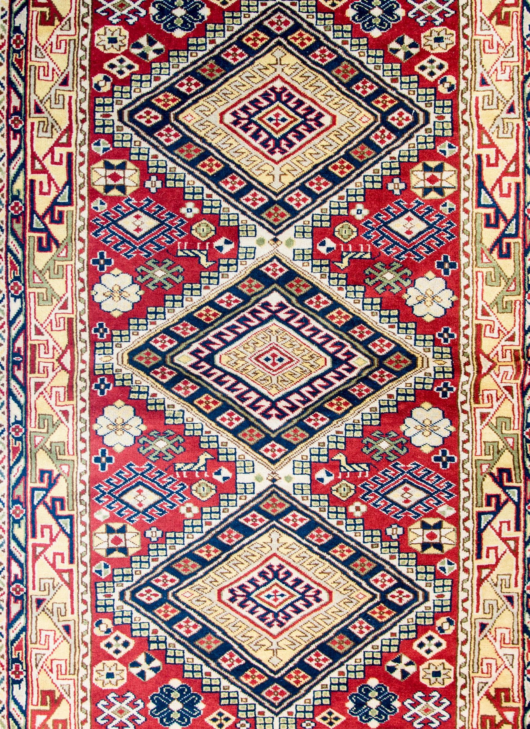 A wonderful vintage Anatolian Turkish rug with three large diamond medallions amidst a crimson field of multicolored flowers and goats. The border is complex with multiple wide and thin geometric stripes with stylized floral and vine patterns.