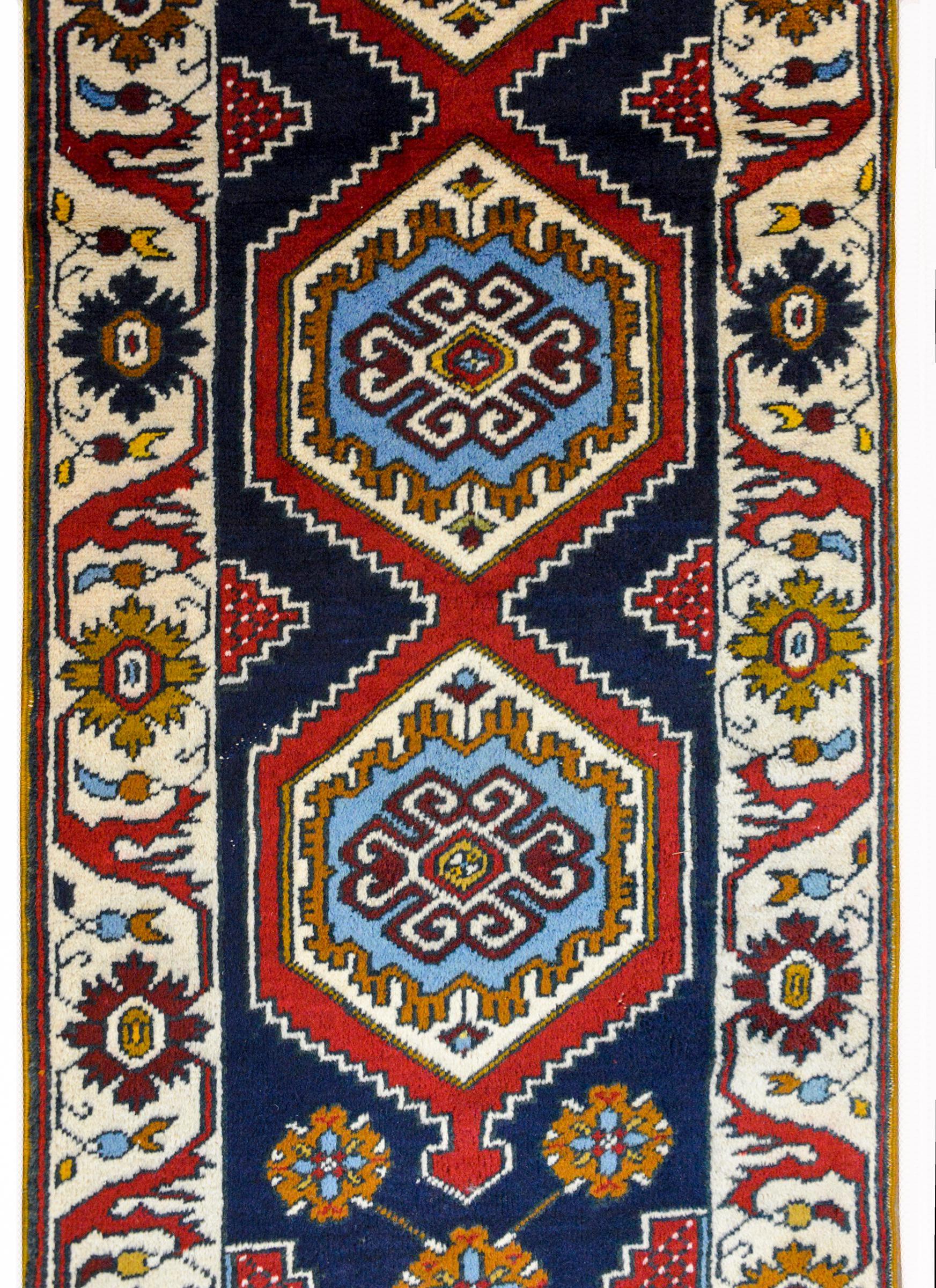 A wonderful 20th century Anatolian Turkish runner with four large boldly partnered medallions woven in brilliant indigo, gold, crimson, and white, set against a dark indigo background and amidst more stylized flowers. The border is bold, with a wide