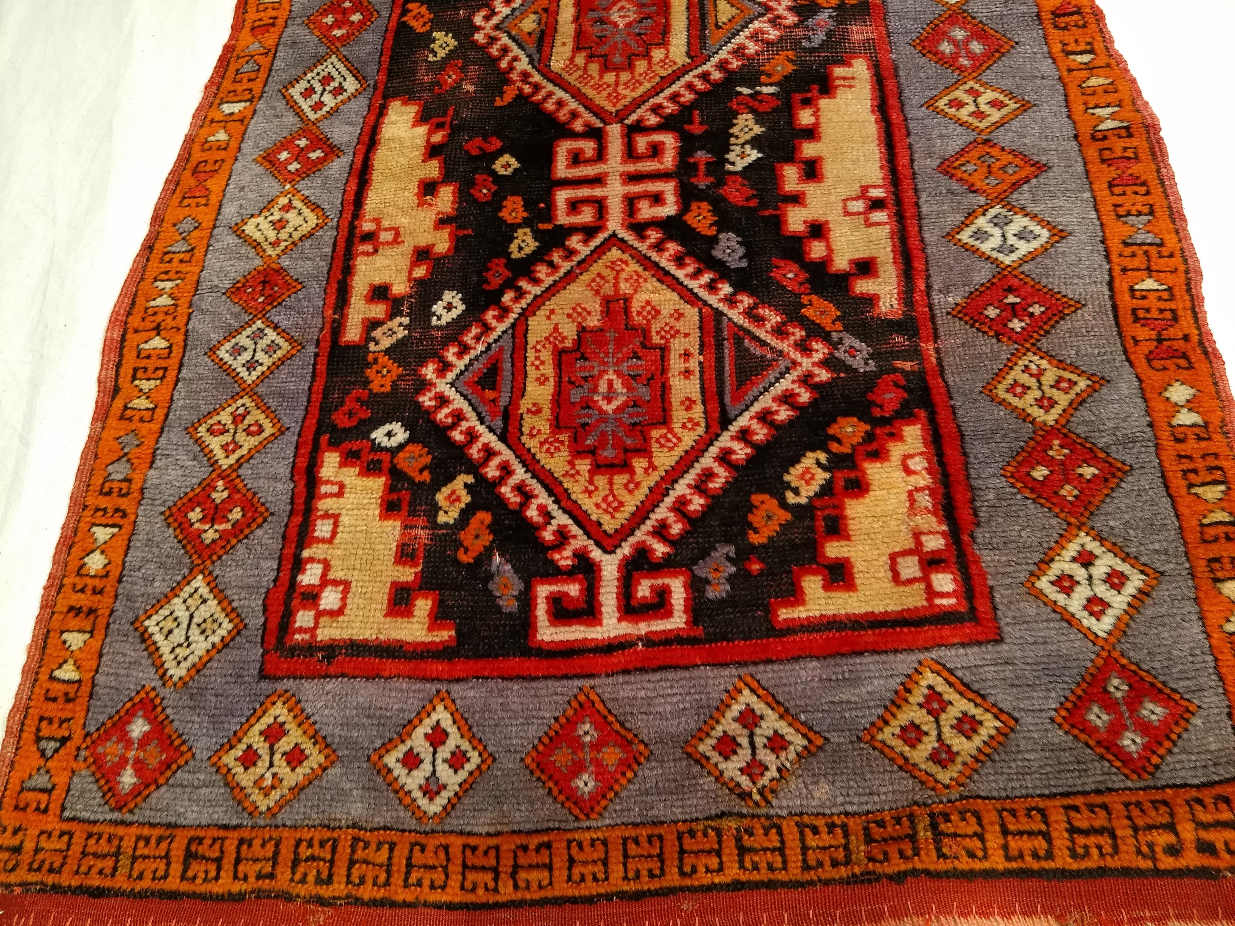 A beautiful Anatolian village rug from the early 1900s. The rug has a two-medallion design set on a navy blue color field. The medallions are red and pale yellow. The rug has a lavender color border with small medallions in pale yellow, orange, and