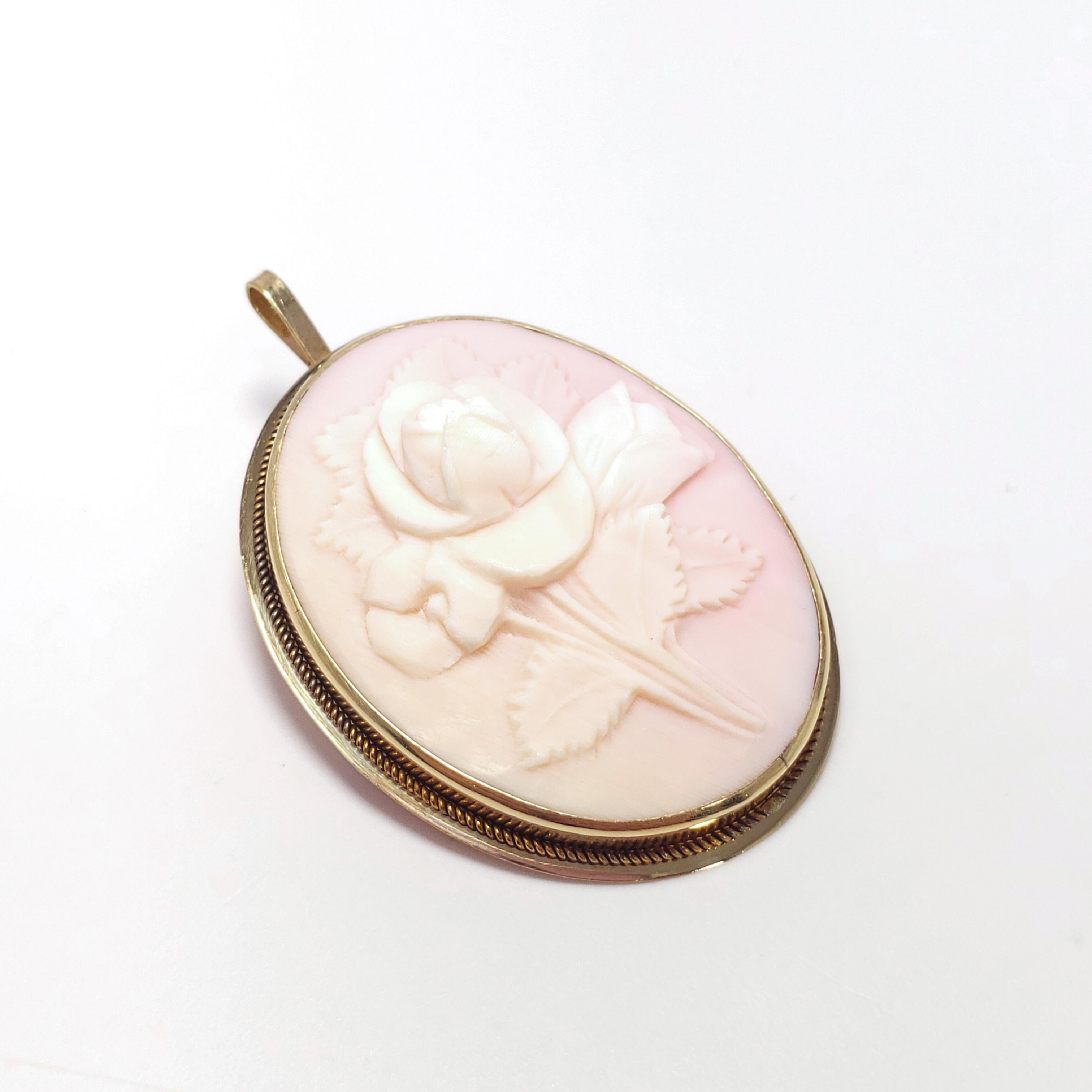 An angel-skin coral cameo that can be worn as both a brooch/pin and a pendant. Real white & soft pink colored angel skin coral. An elevated floral bouquet motif is carved in the coral, set in an accented, open back, 14K gold bezel. A quintessential