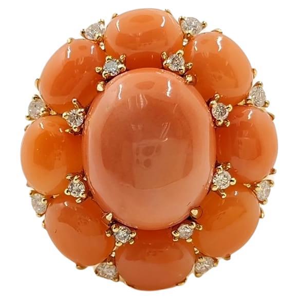 Presenting our captivating Coral Ring, set in 18 Karat Yellow Gold. This striking piece features an eye-catching 6.85 carat oval cabochon coral centerpiece, surrounded by eight additional corals totaling 7.1 carats. The ring's vibrant coral ensemble