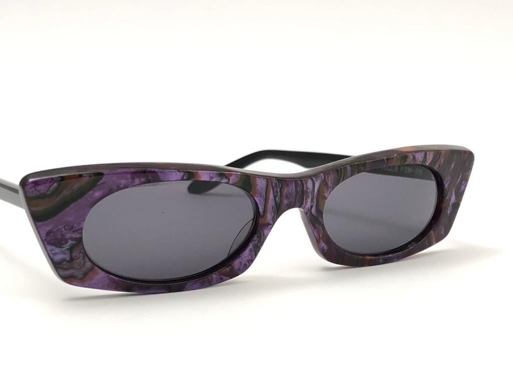 Sleek purple pair of sunglasses signed by English Anglo American Optical.  
Spotless pair of dark grey lenses. 
Made in England.

This pair has minor sign of wear consistent with age and storage.


FRONT  12.5 CMS
LENS HEIGHT 2.4 CMS
LENS WIDTH 4.4