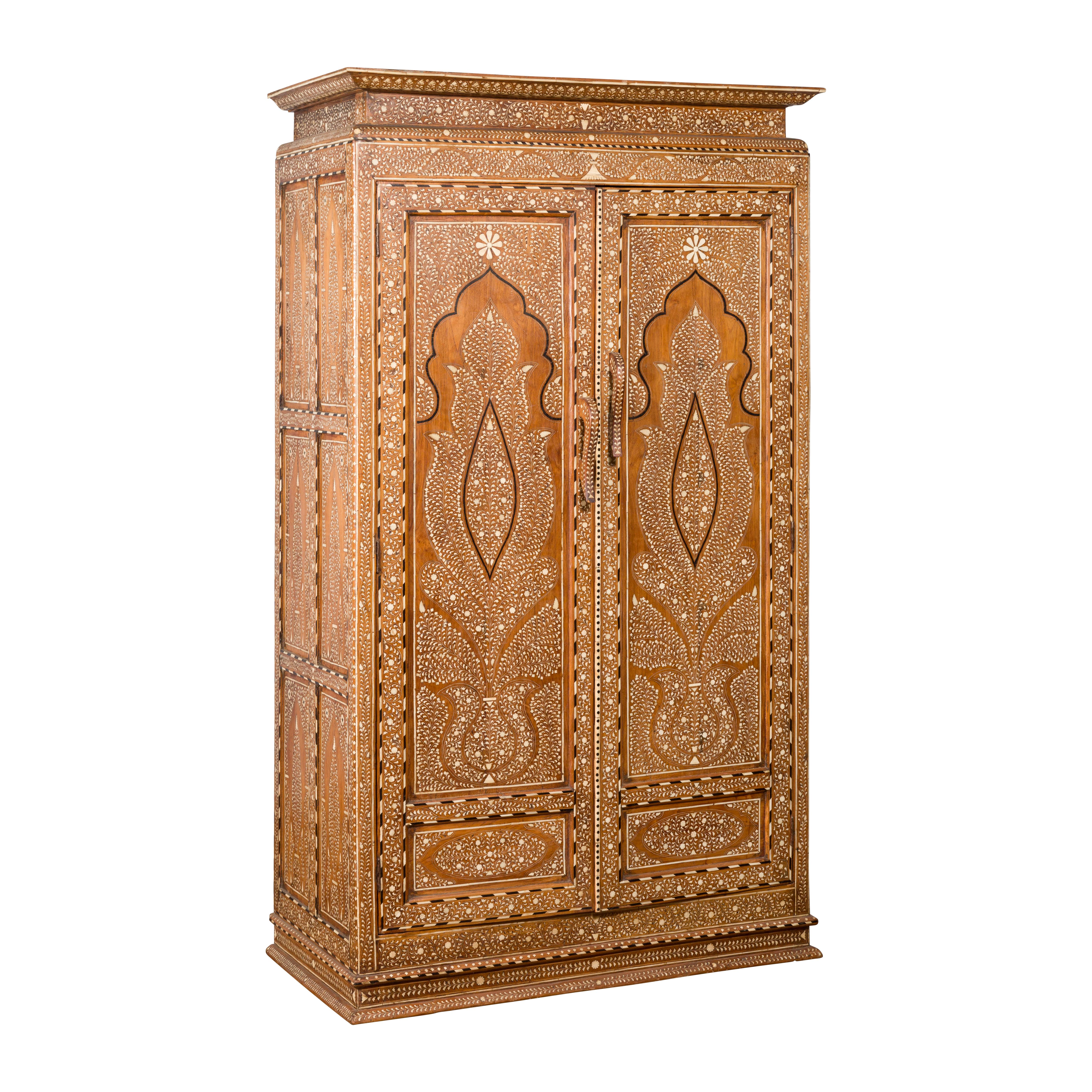 A vintage Anglo-Indian inlaid wooden wardrobe cabinet from the mid-20th century, with ebonized accents, bone and horn inlay. Capturing our attention with its intricate decor, his tall cabinet is adorned with an abundant decor of foliage and