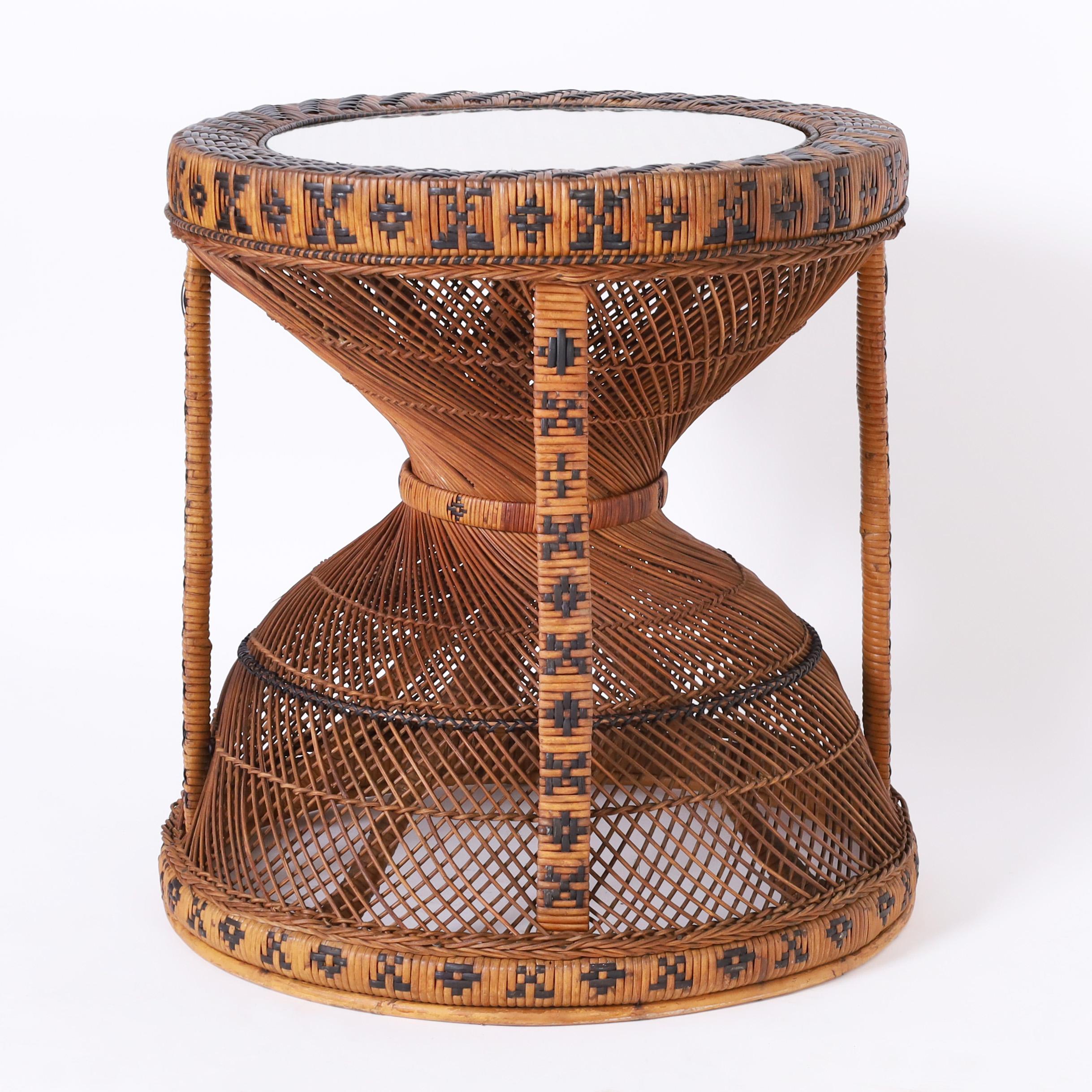 Standout vintage Anglo Indian stand handcrafted in wicker and reed over a wood frame with a caned top under inset glass over an hourglass form base decorated with geometric symbols.