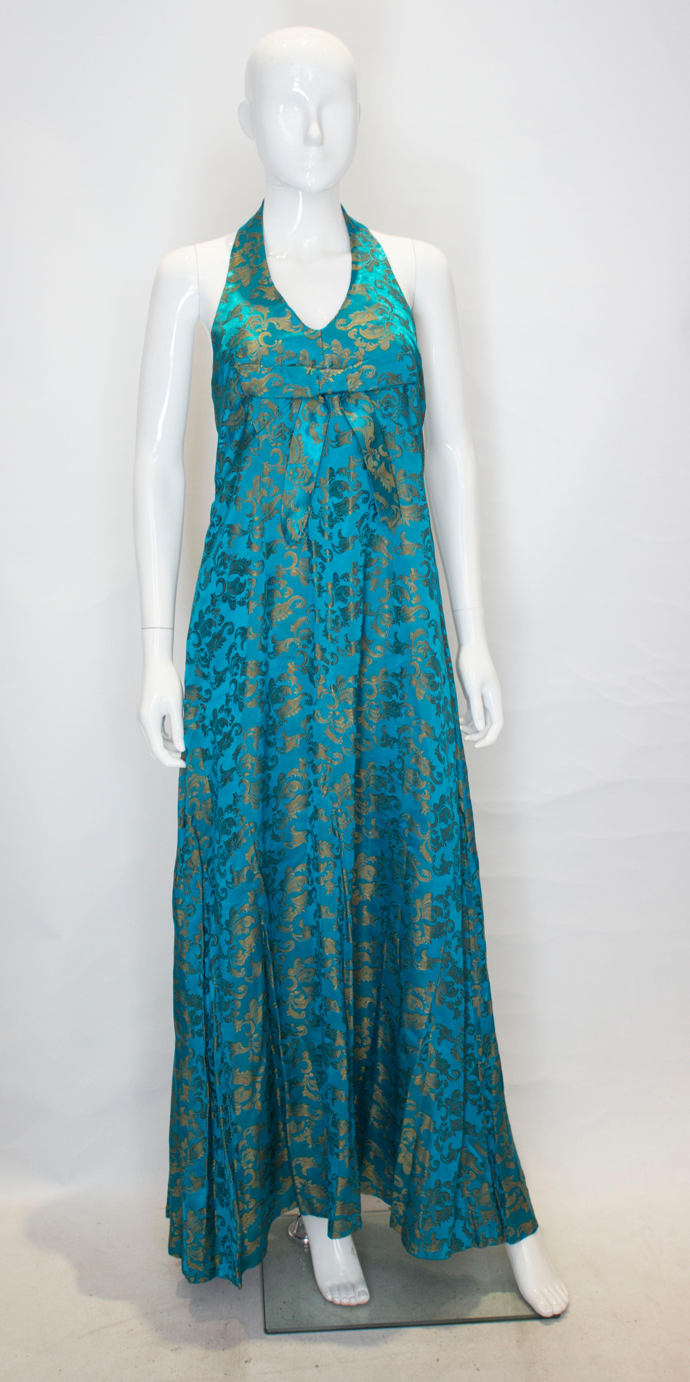 A vintage halter neck gown by Anna Clay Couture. The dress is in a brocade like fabric with button fastening at the neck and a central back zip. It has bow detail and bust leval.