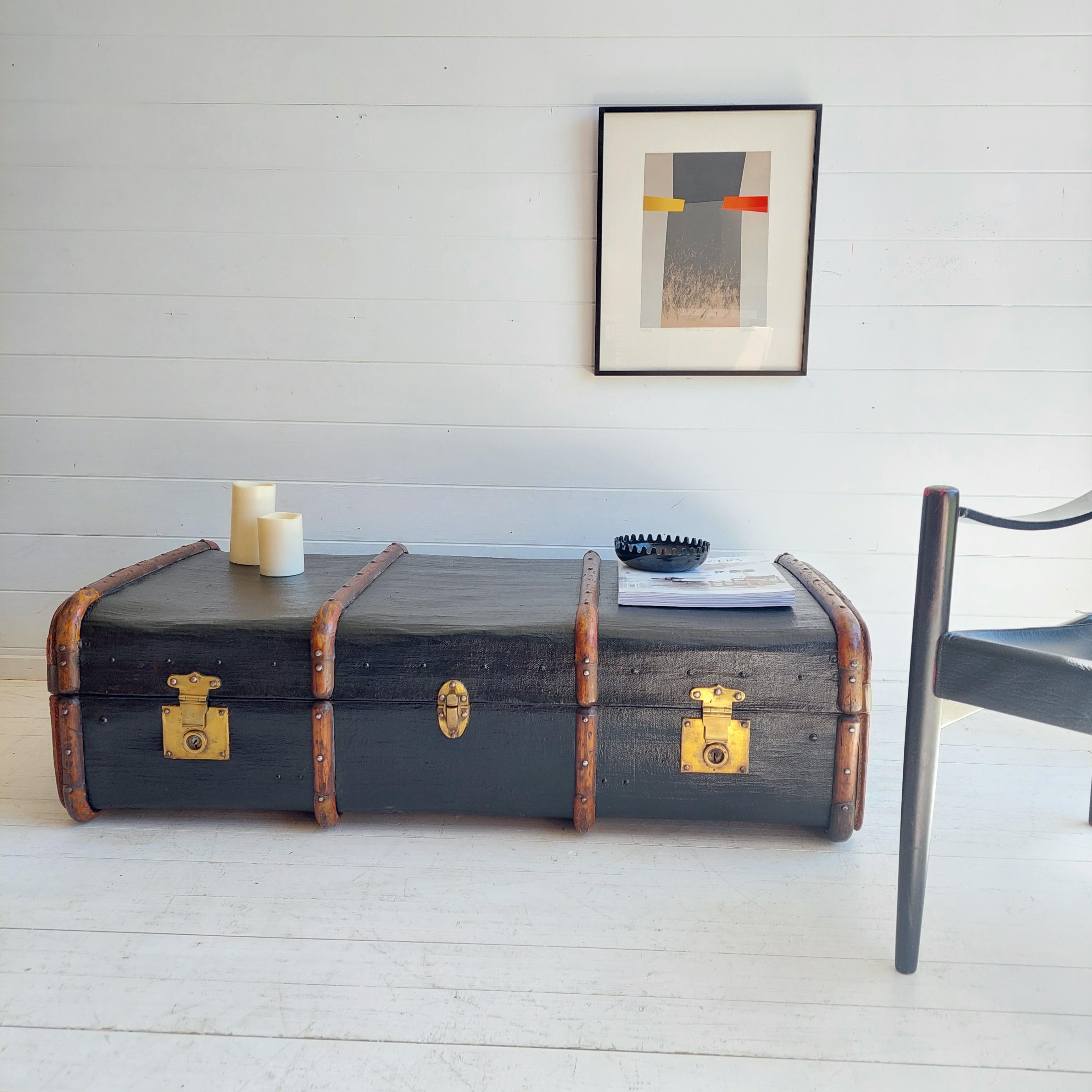 A great 1930s large black hardboard and wood banded travel trunk.

smartly wooden bars
Its adorned with solid polished brass fixings, thick leather handles on each side. 
Metal protections in order to be stackable without doing any damage.