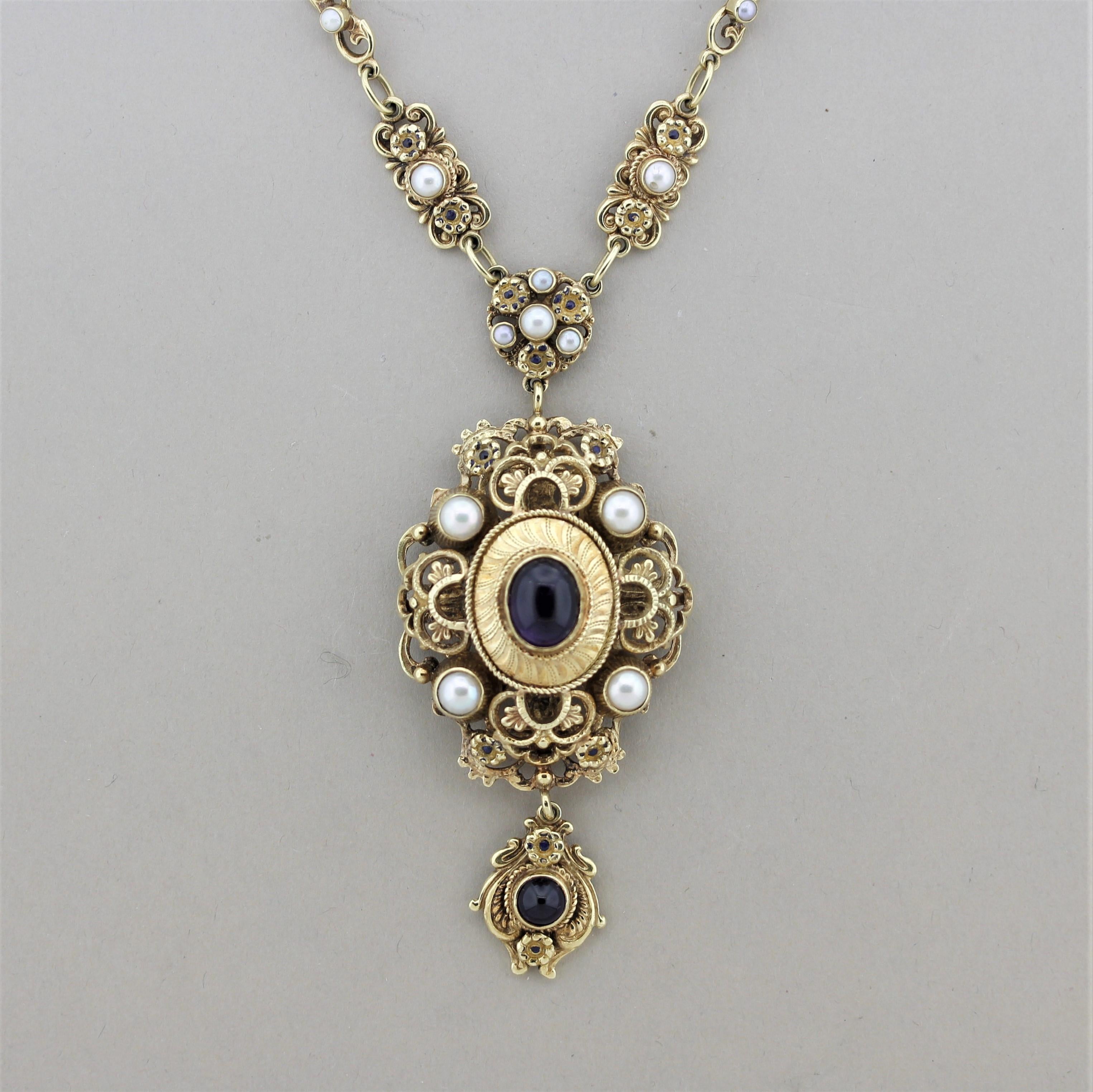 A large vintage gold necklace made in the antique-style with Victorian features. The necklace showcases two amethyst cabochons along with multiple pearls set along the necklace. There is filigree goldwork as well as millgrain which are classic