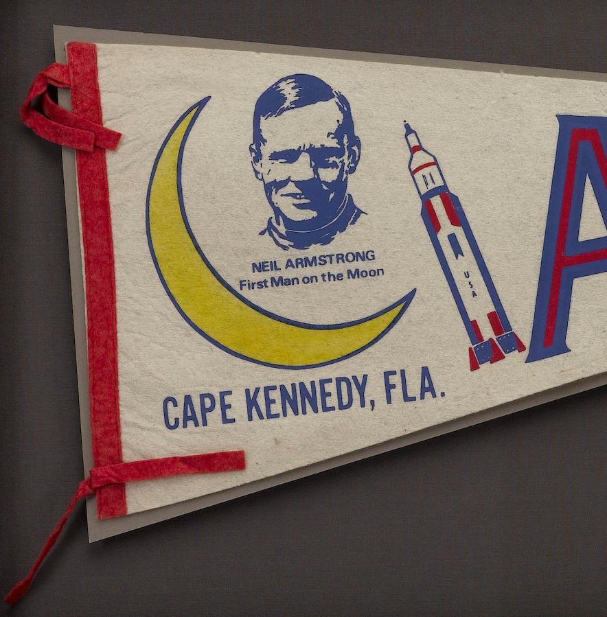 Presented is a vintage pennant from 1969 highlighting the Apollo 11 space mission. The felt pennant features a white field with the words 