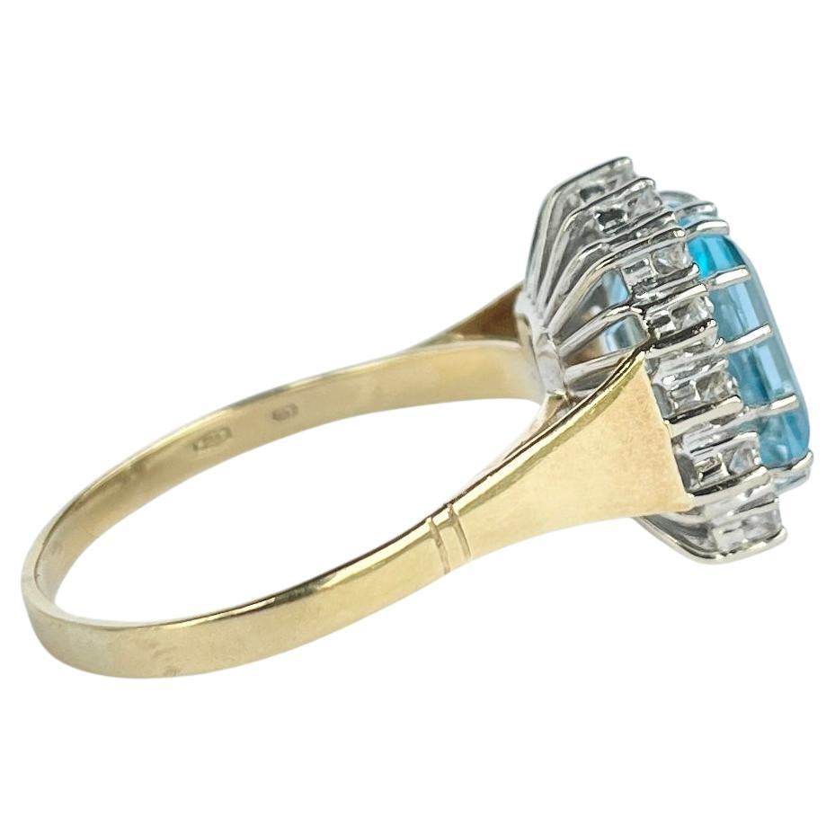 In der Mitte dieses wunderschönen Clusterrings sitzt ein funkelnder Aquastein. Um den 5 1/2ct Aqua Stein sitzt ein Halo aus kleineren Diamanten, die jeweils etwa 4pts messen. Der Ring ist aus 18 Karat Gold modelliert und die Steine sind in Platin