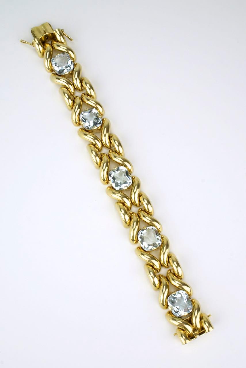 An aquamarine and 14k yellow gold fancy link bracelet with five pale blue cushion cut aquamarine stones of very good clarity claw set in a knot link motif bracelet with a box clasp and two figure of eight safety clasp closures.  This Luxe bracelet