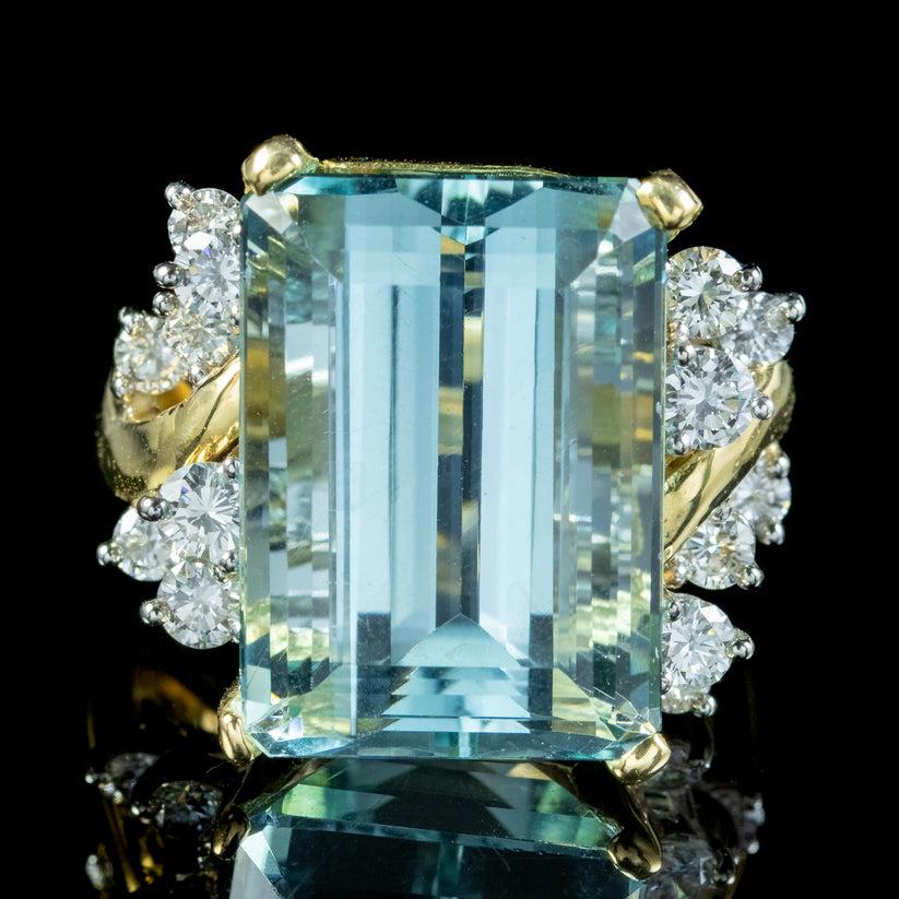 A magnificent vintage cocktail ring showcasing a breath-taking emerald cut aquamarine weighing approx. 17ct. It has a beautiful, clear blue hue with flashes of green and is complemented by fourteen bright brilliant cut diamonds on either side