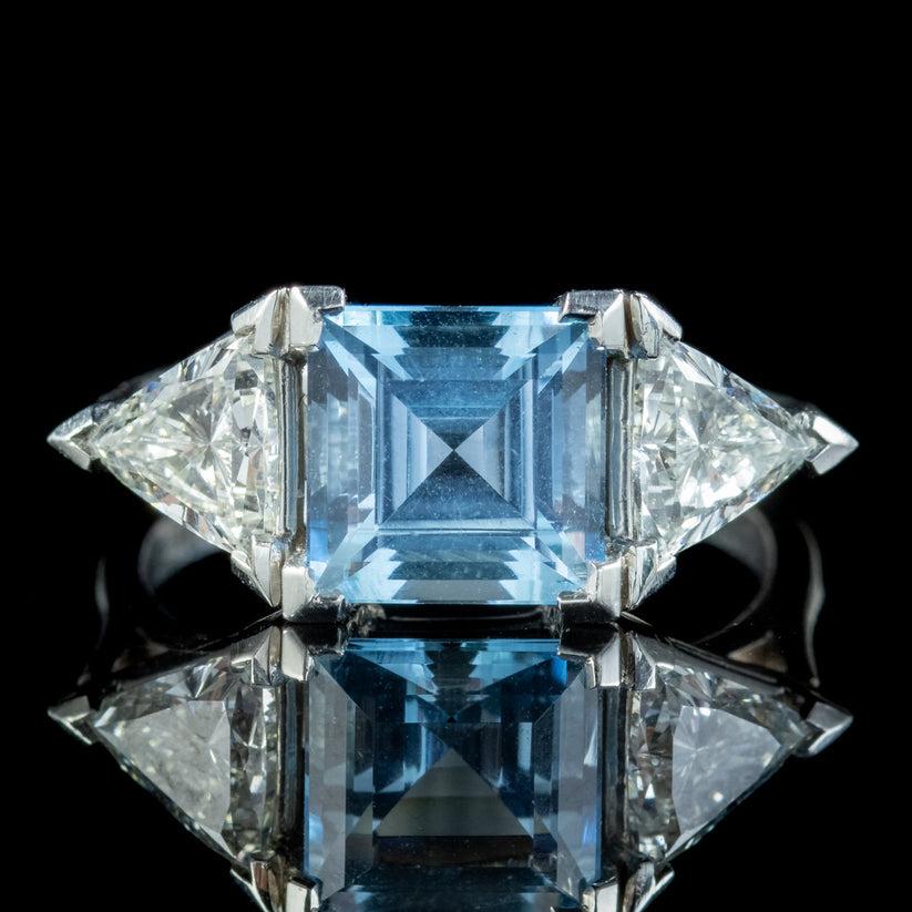 Ein wunderschöner Vintage-Trilogie-Ring mit einem klaren blauen Aquamarin im Carrs-Schliff in der Mitte mit einem Gewicht von ca. 3 ct. und zwei schillernden Diamanten im Trillion-Schliff auf jeder Schulter.

Die Diamanten sind jeweils ca. 0,90ct
