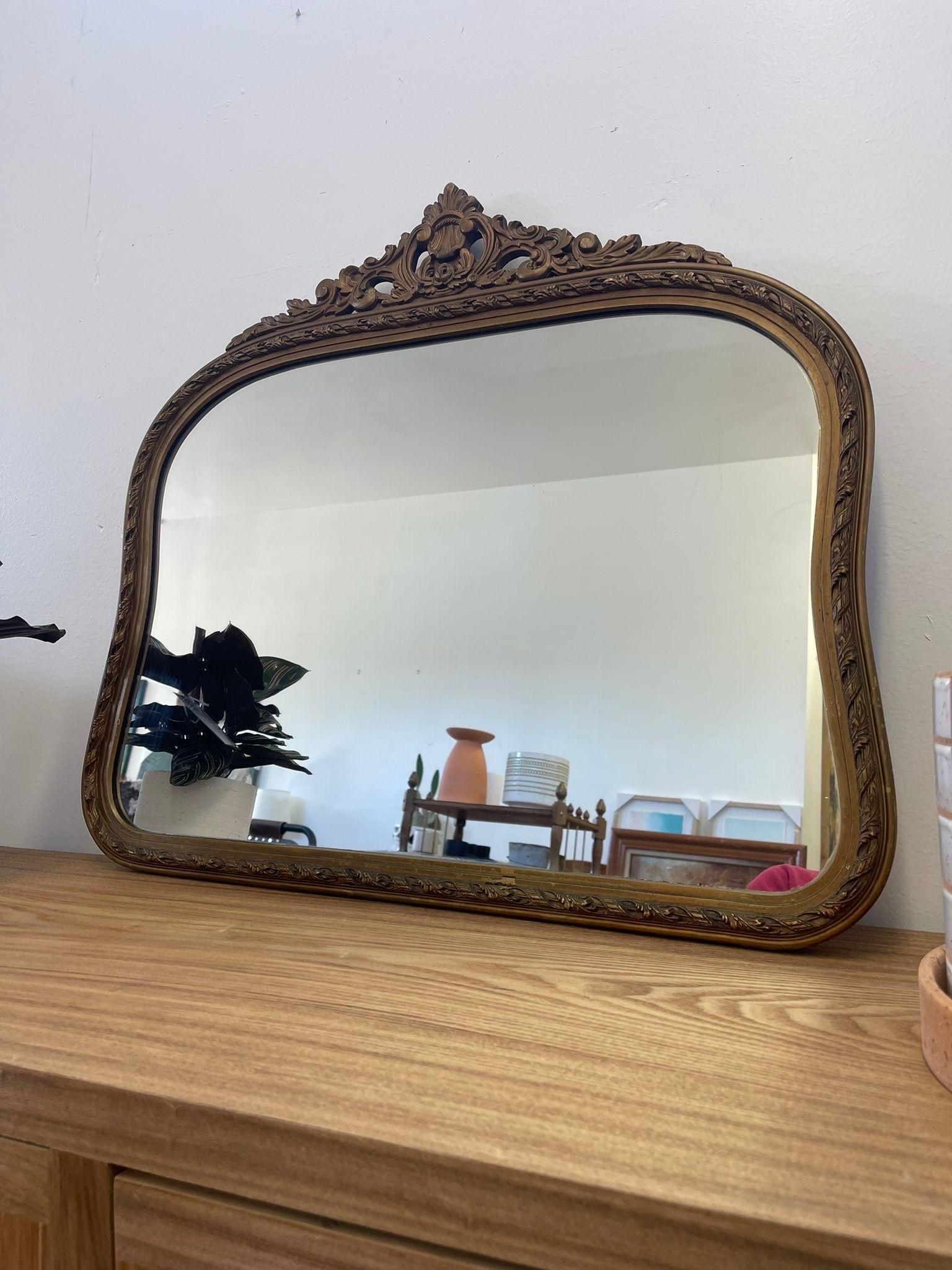 Dieser Spiegel hat eine wunderschöne, einzigartige Form mit einer gewölbten Oberseite und einer leichten Biegung an den Seiten. Abgerundeter Rand auch an der Unterseite. Der geschnitzte Holzrahmen ist mit einem Goldton bemalt. Der Stempel auf der