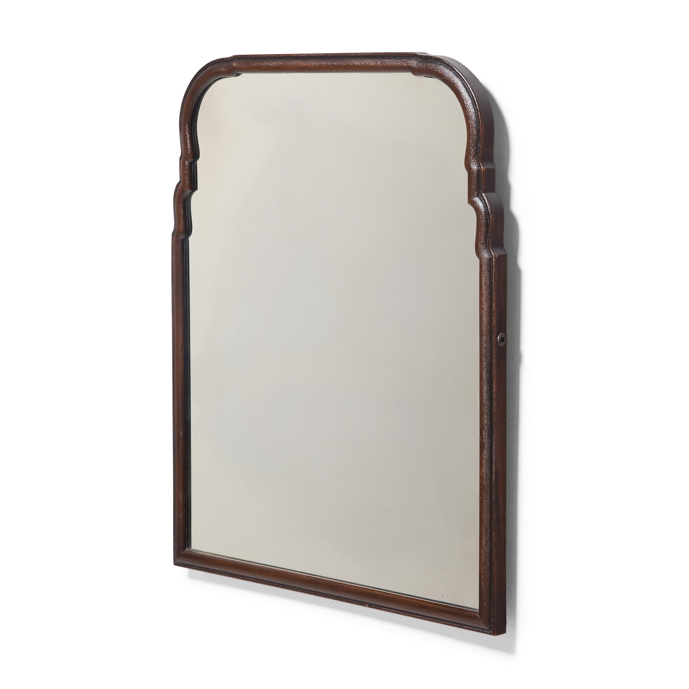 This elegant vintage wall mirror is enclosed by a narrow hardwood frame and features an arched top with sinuous, stepped corners. The rounded frame is stained dark brown and finished with a beaded edge. Years of use have imparted a rich patina and