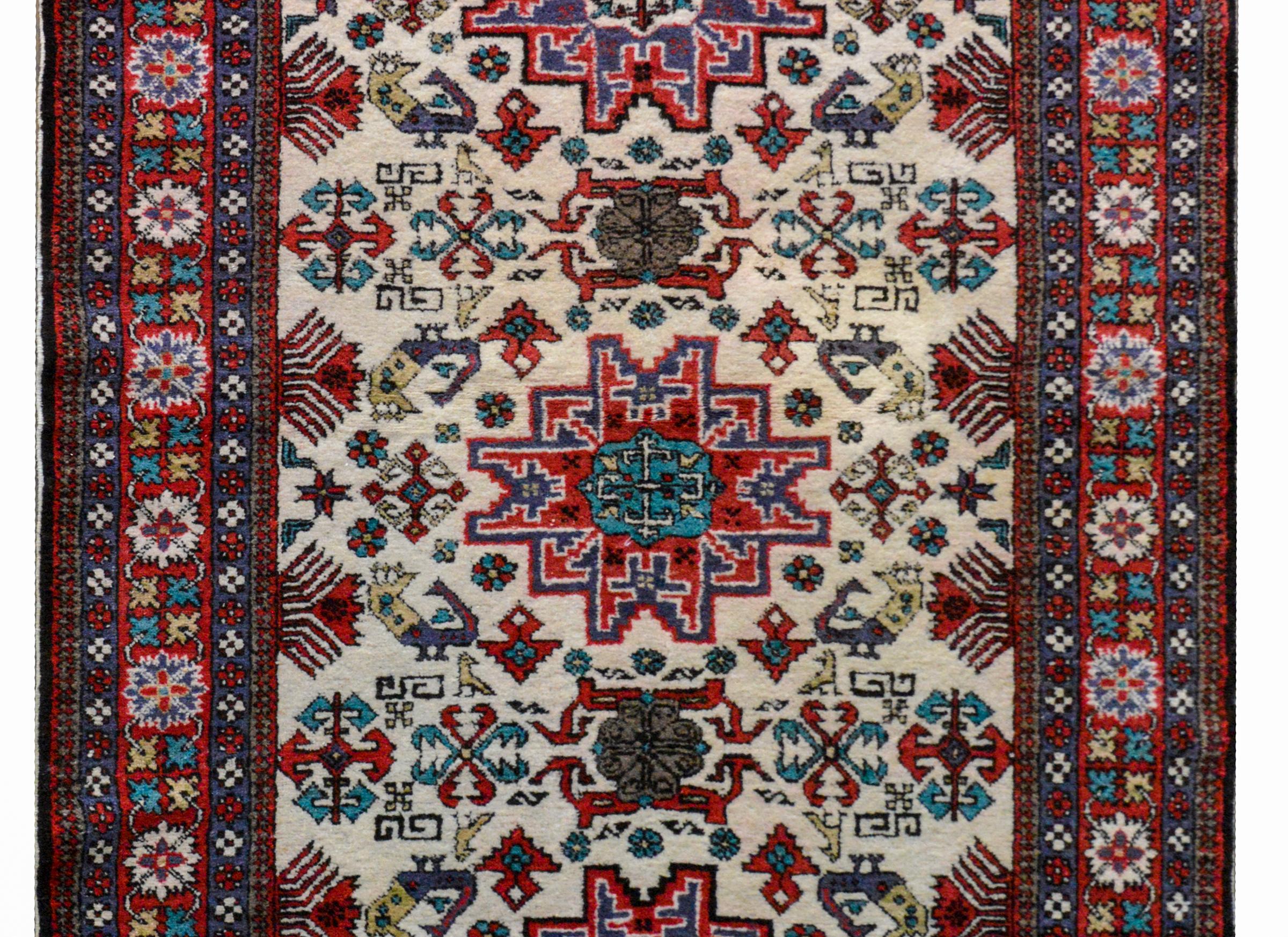 A vintage Persian Ardabil rug with a tribal pattern woven with stylized flower and birds woven in crimson, teal, and yellow against a white background. The border is wide with a central floral partnered stripe flanked by a pair of petite geometric