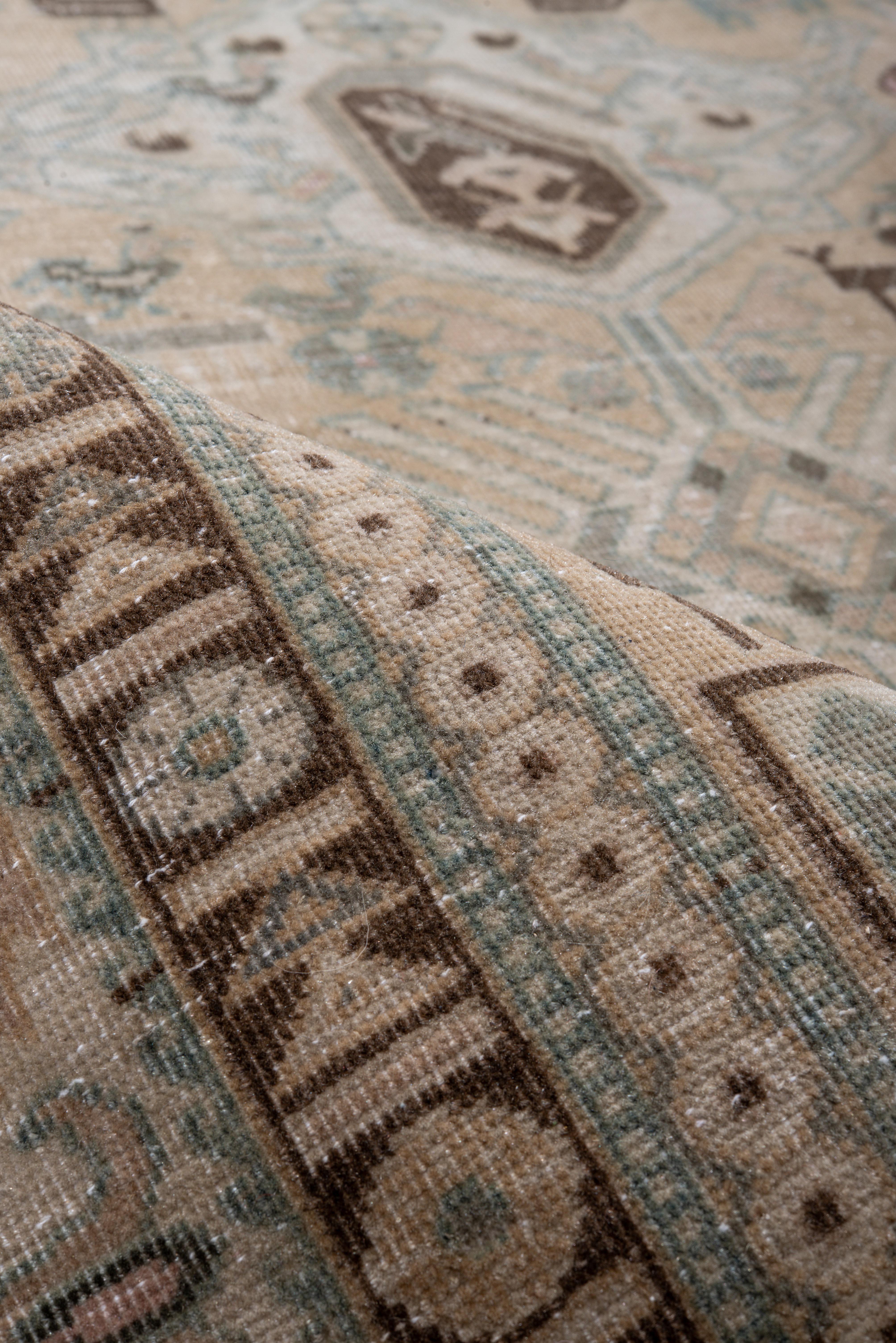 This vintage Ardebil rug features a structured tribal lattice across a soft camel field, punctuated by shield medallions, geometric rosettes, and stylized animal motifs. The design is executed in shades of sky blue, ivory, and mocha, giving the rug