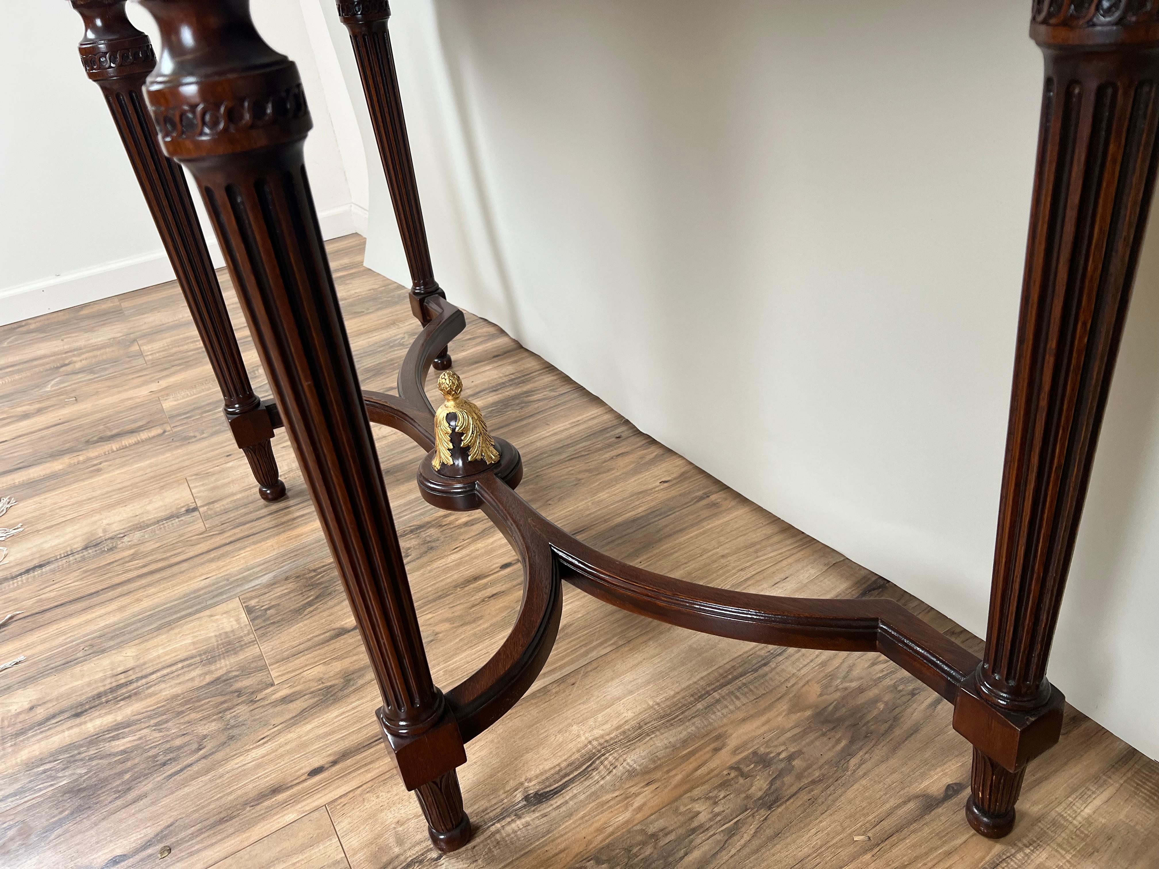 This refined console table by Ardley Hall embodies the grace and symmetry of neoclassical design with a sophisticated blend of materials and craftsmanship. The piece features a smooth granite top resting above an elegant mahogany frame, richly