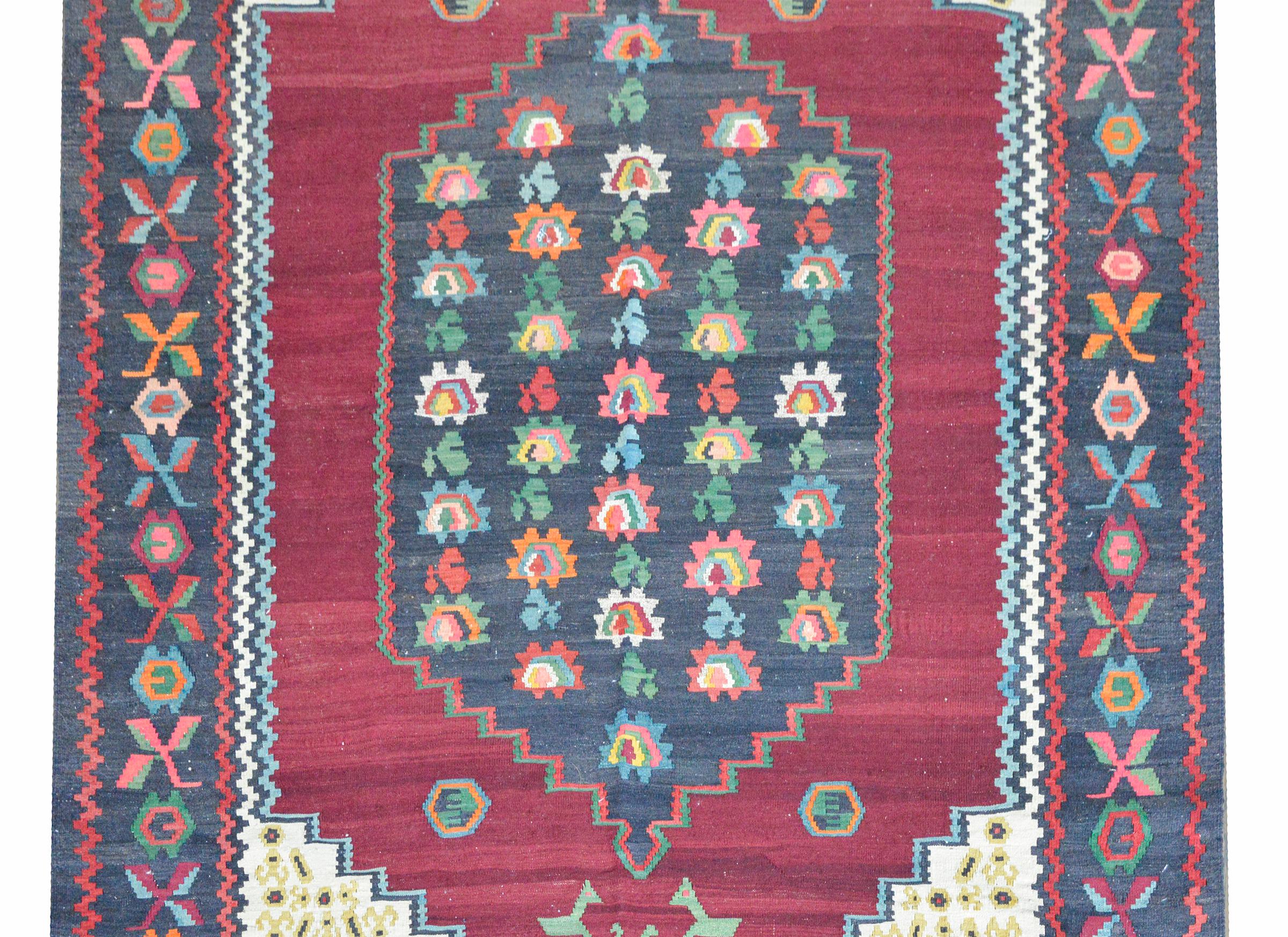 A wonderful vintage Armenian kilim rug with a central medallion with stylized flowers woven in myriad colors against a dark crimson background, and floating amidst a field of more stylized flowers, and surrounded by a wide border with more flowers.