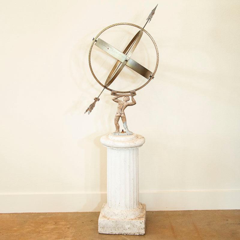 This vintage painted globe shaped garden ornament, called an armillary, is made up of metal bands, pierced by an arrow and supported by a mounting bracket. The base is an image of Atlas holding up the world. These 