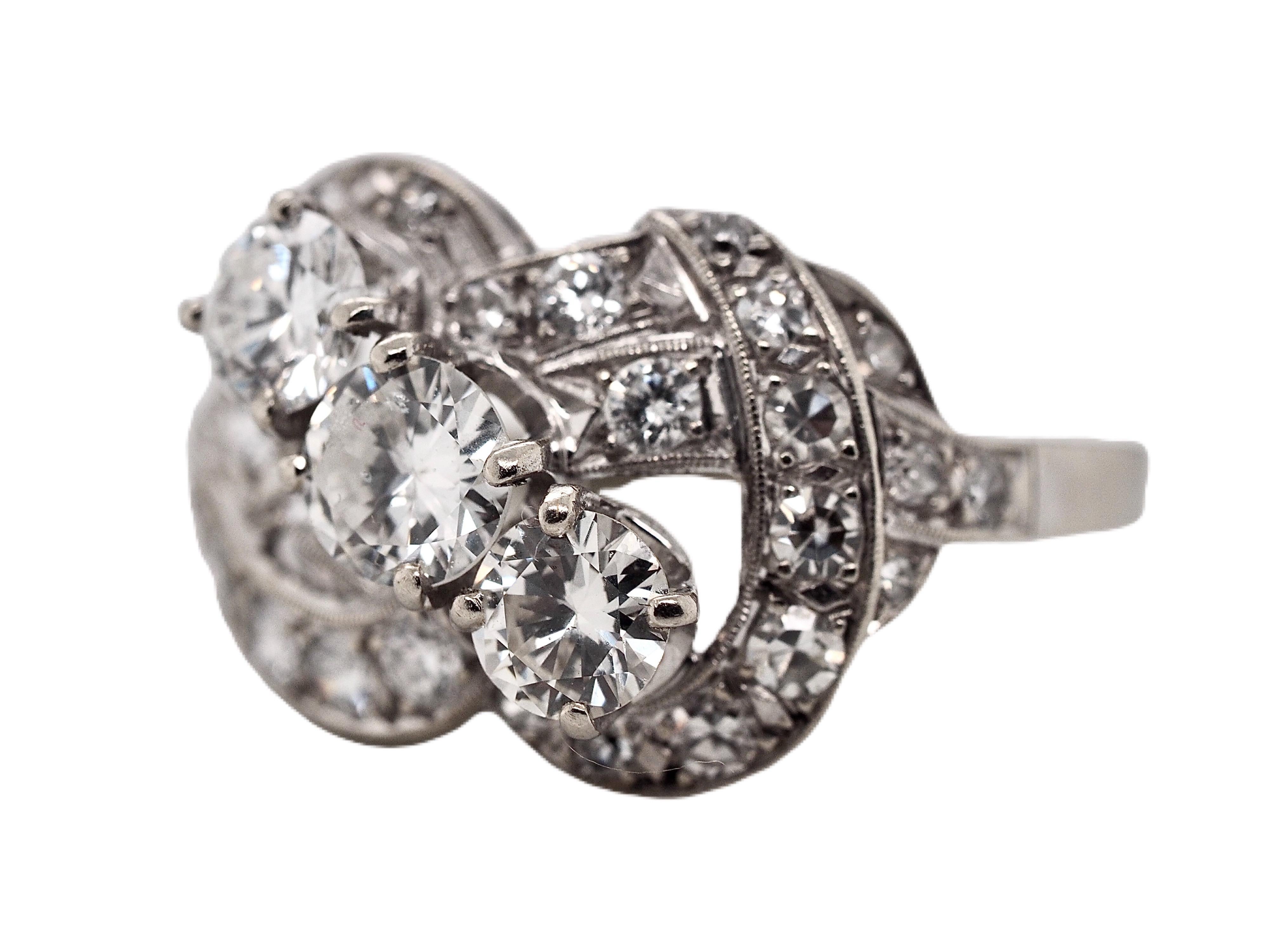 This incredible 14 karat white gold vintage three stone ring dates back to the 1930's. It features three round brilliant cut diamonds diagonally set in four prong settings, weighing approximately 1.07 carats total. The center diamonds are accented