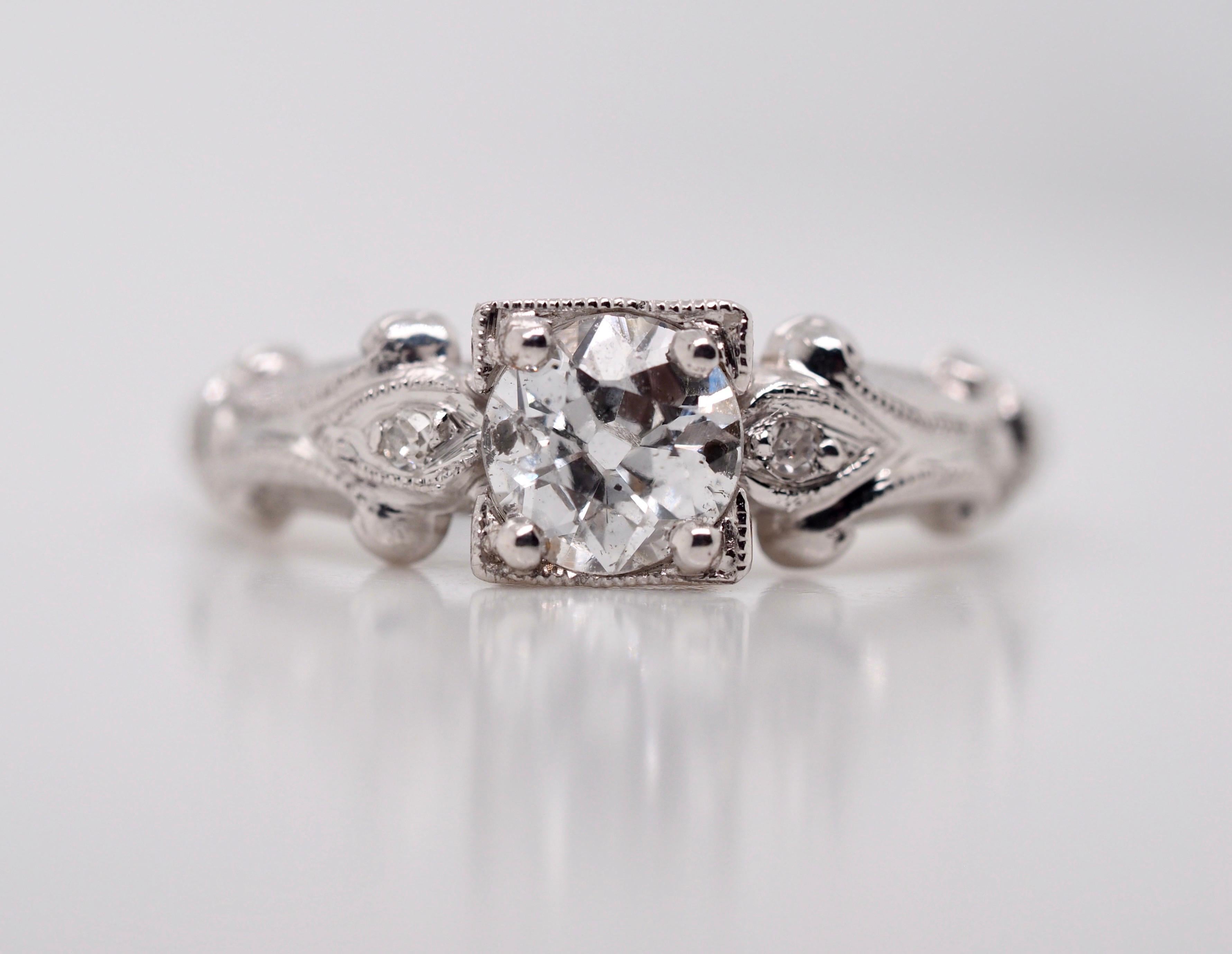 This gorgeous 14 karat white gold Art Deco vintage engagement ring features an Old European Cut Diamond set in four prongs, weighing 0.44 carats, I1 in clarity I in color. Two old mine cut diamonds are accenting the sides with adorned swirls flowing