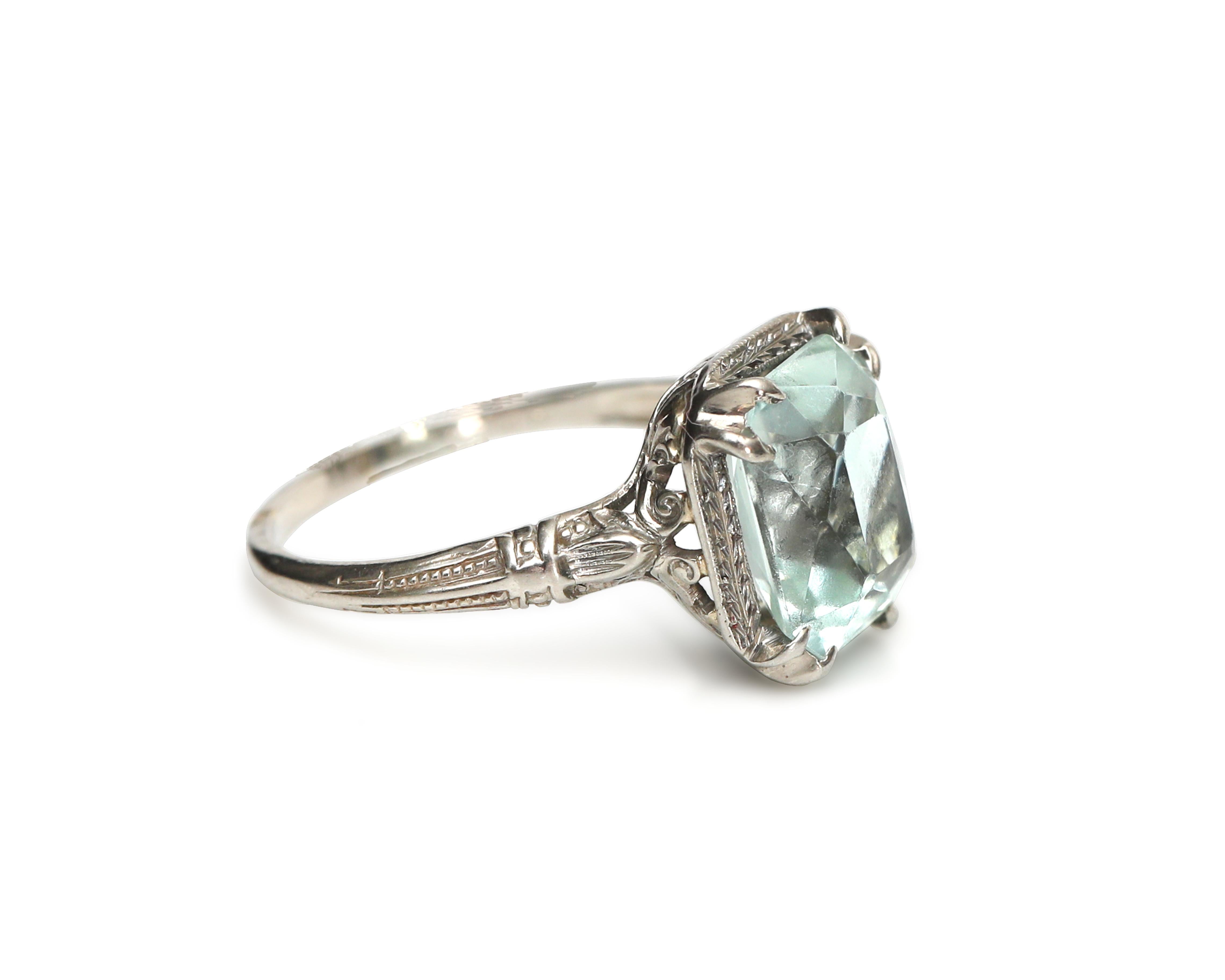 Description: 
This 1920's fashion ring is a genuine Art Deco beauty! The 18K white gold band showcases intricate work around the shoulders of the ring and features a transparent blue/green 4.2 Carat Aquamarine. The lovely gem is held by 4 double