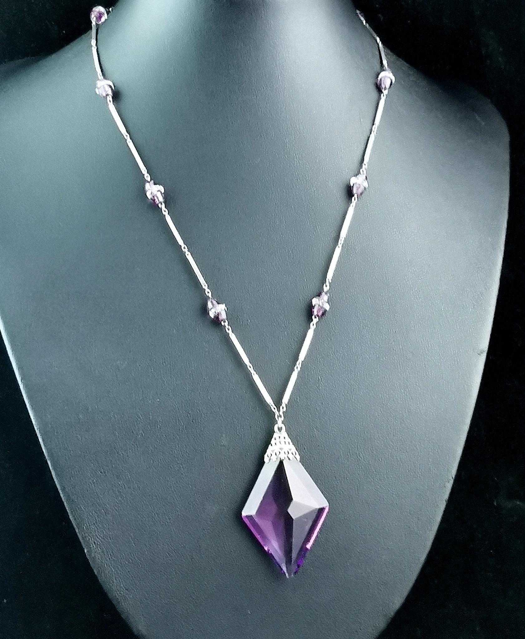 A gorgeous vintage Art Deco era Amethyst glass pendant or drop necklace.

It is a station style necklace with small Amethyst glass beads and faceted clear paste beads stationed along a fancy bar link necklace.

The necklace has a large faceted