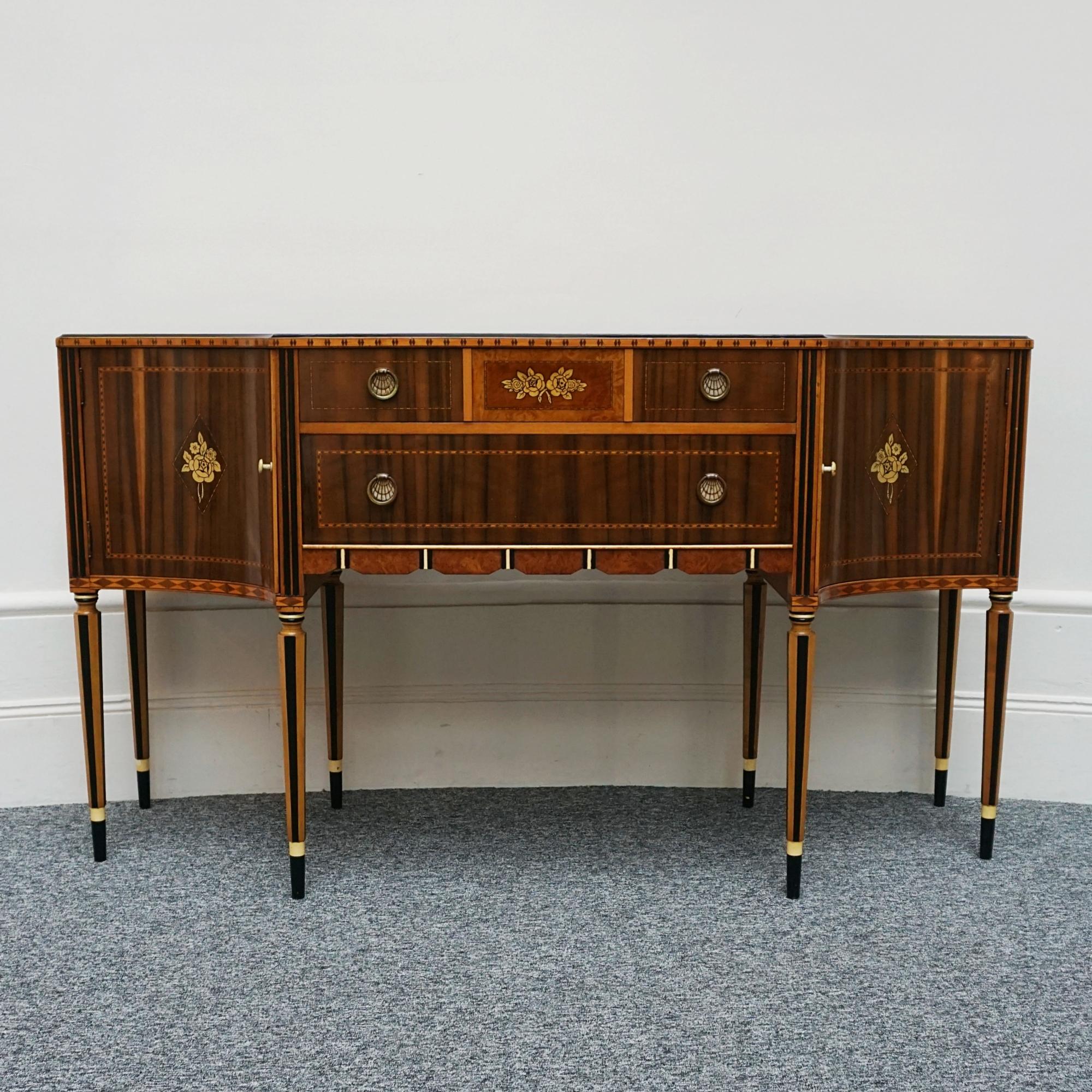 An Art Deco Sideboard on tapered legs. Two central drawers flanked by curved cupboard sections. Australian walnut veneered with ebonised and satinwood inlay and original brass handles with ivorine decoration.
