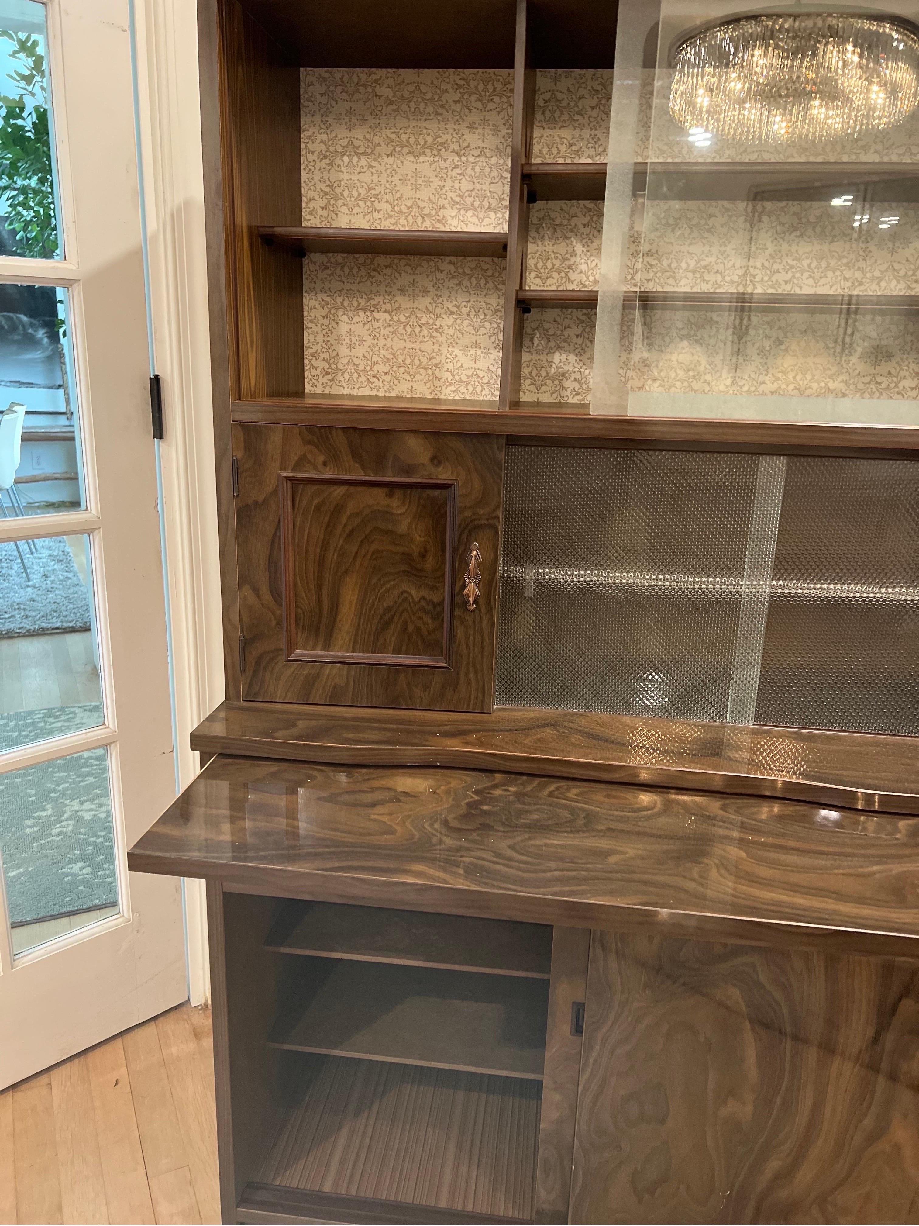 Unique small scale Art Deco Cabinet with high gloss veneer.  Has a small pull out shelf for making cocktails.  
Lower half has two sliding doors with shelves for storage.  Upper half includes glass sliding doors for barware, glasses and decanters. 