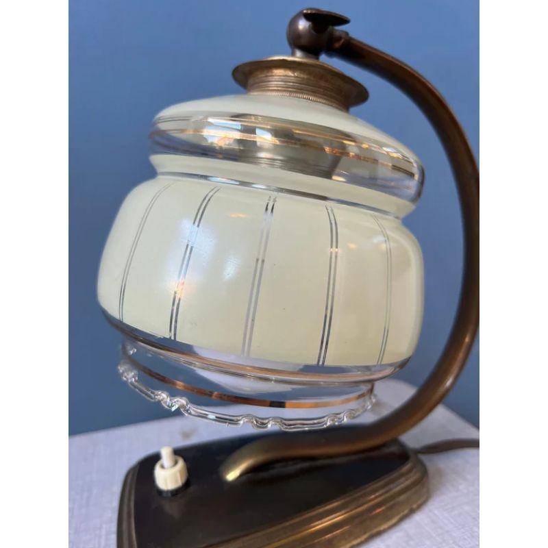 Art deco Nachttischlampe mit Glasschirm. Die Lampe hat einen bronzefarbenen Sockel und einen Glasschirm. Die Lampe benötigt eine E14-Glühbirne und hat derzeit einen EU-Stecker.

Abmessungen:
ø Schirm: 13 cm
Höhe (einstellbar): 24 cm

Zustand: Sehr