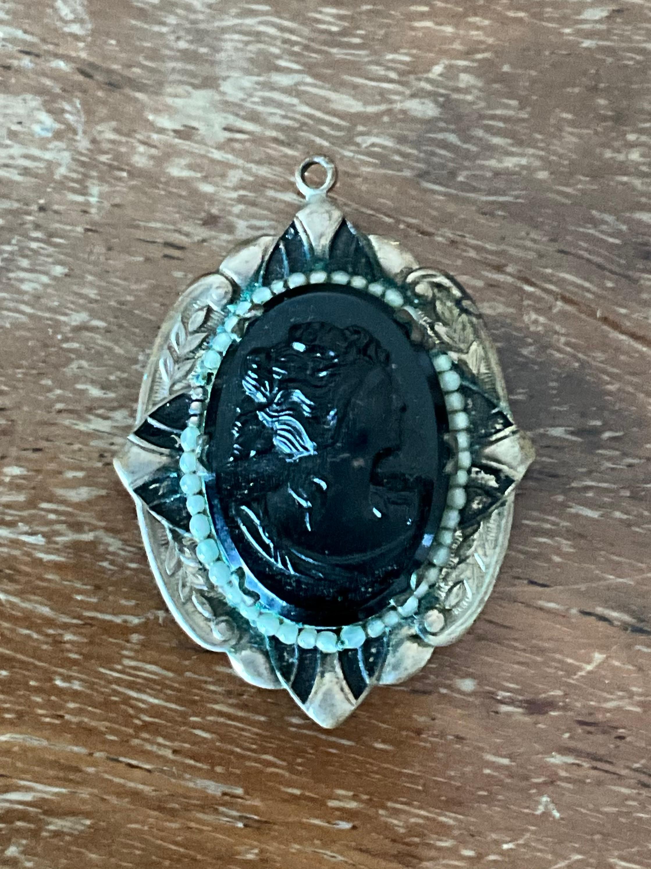 Embrace timeless elegance with this vintage Art Deco black cameo locket pendant. Featuring a beautifully raised profile of a classical lady in striking black and ivory tones, the cameo is set within an ornate, geometric locket design characteristic
